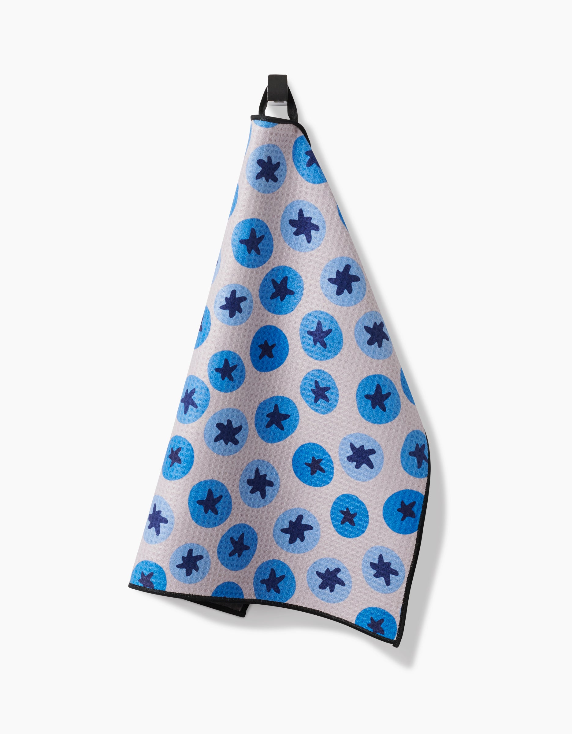 The Geometry Sweet Blueberries towel, in light grey with blue circles featuring dark blue airplane silhouettes, hangs by a black loop against a plain white background.