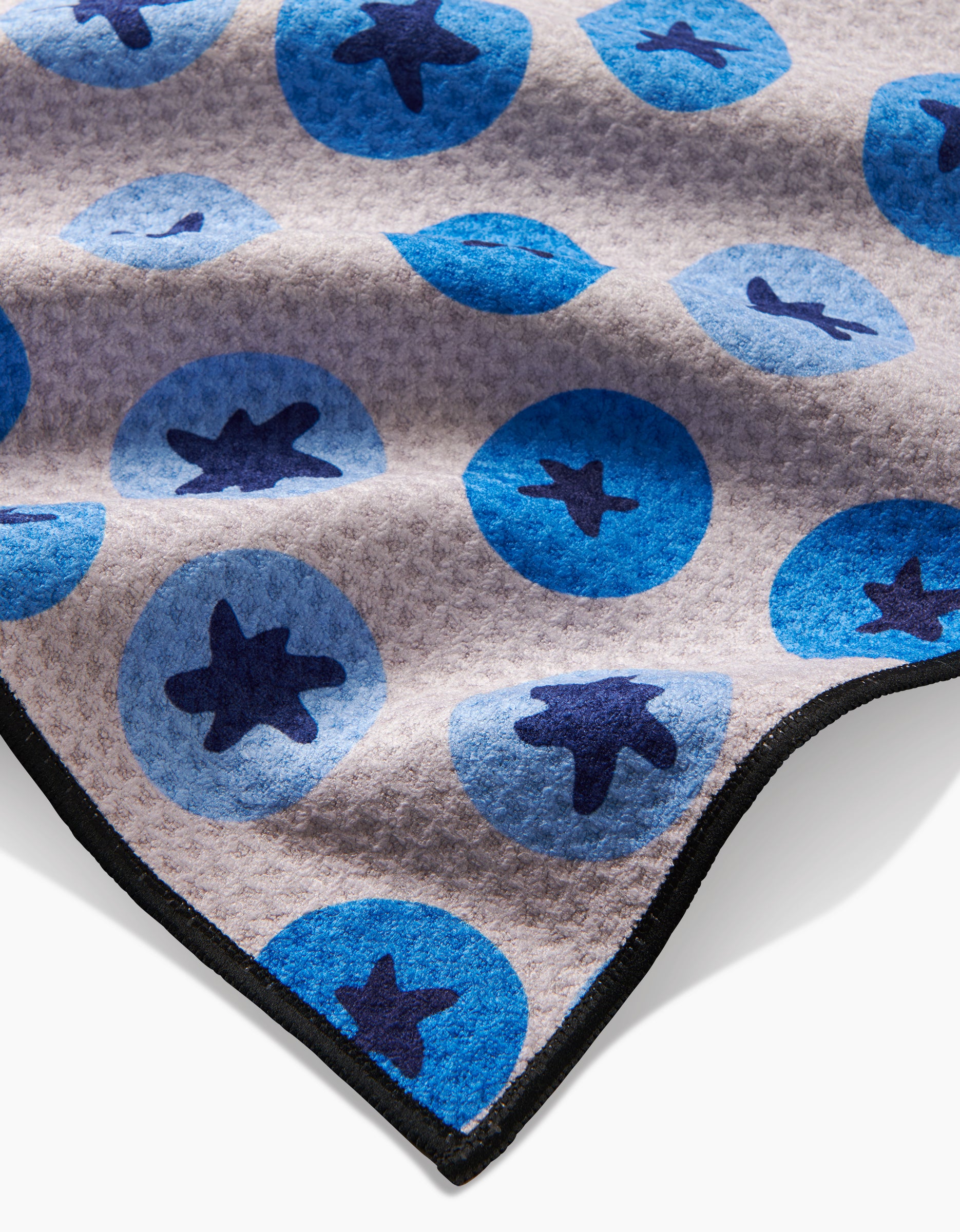 A close-up of the Geometry Sweet Blueberries ultra-absorbent blanket featuring blue circles and dark blue starfish on a light gray background, finished with a black edge trim for added style.