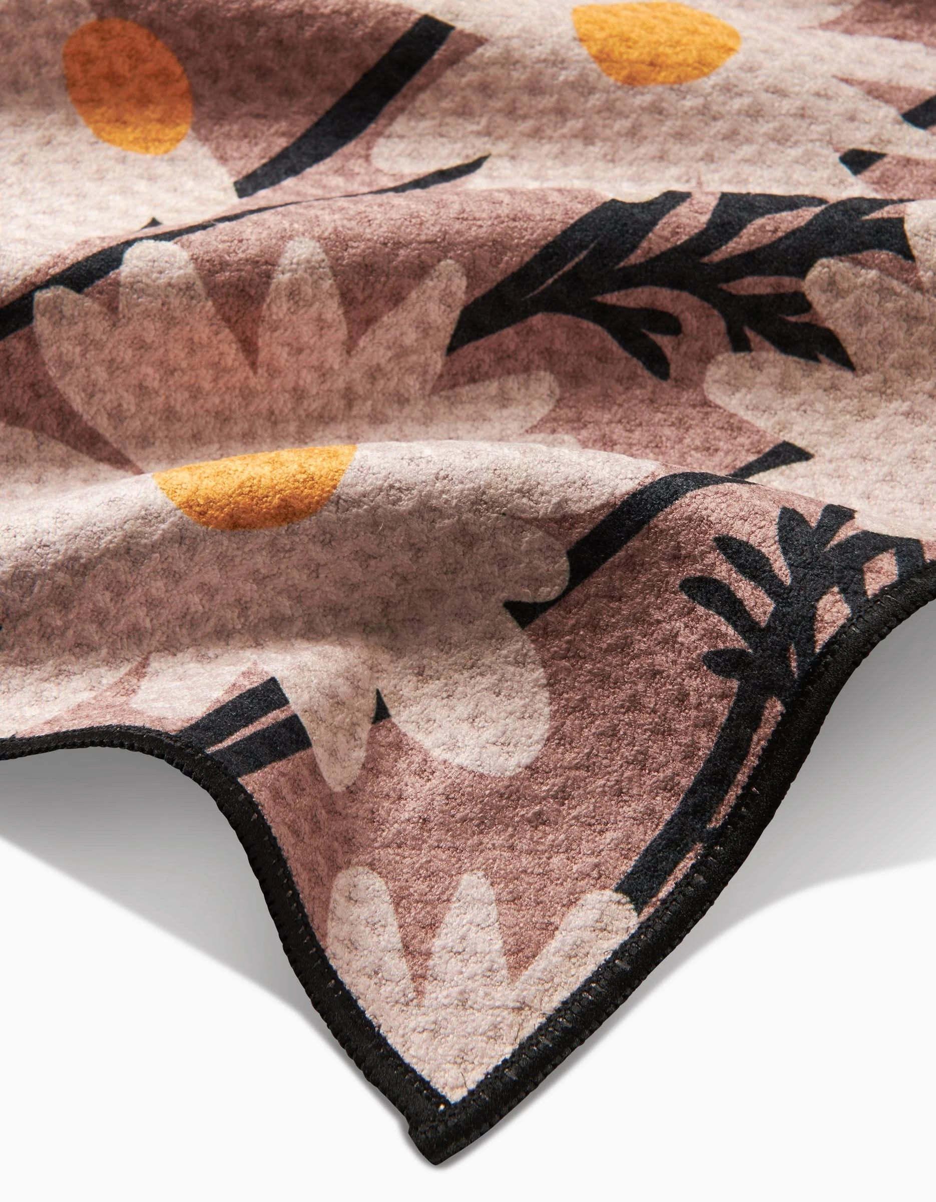 A close-up of Geometrys Sweet Daisies Paw Towel, a soft, ultra-absorbent blanket with large white daisies and yellow centers on a light brown background, finished with a neat black edge.