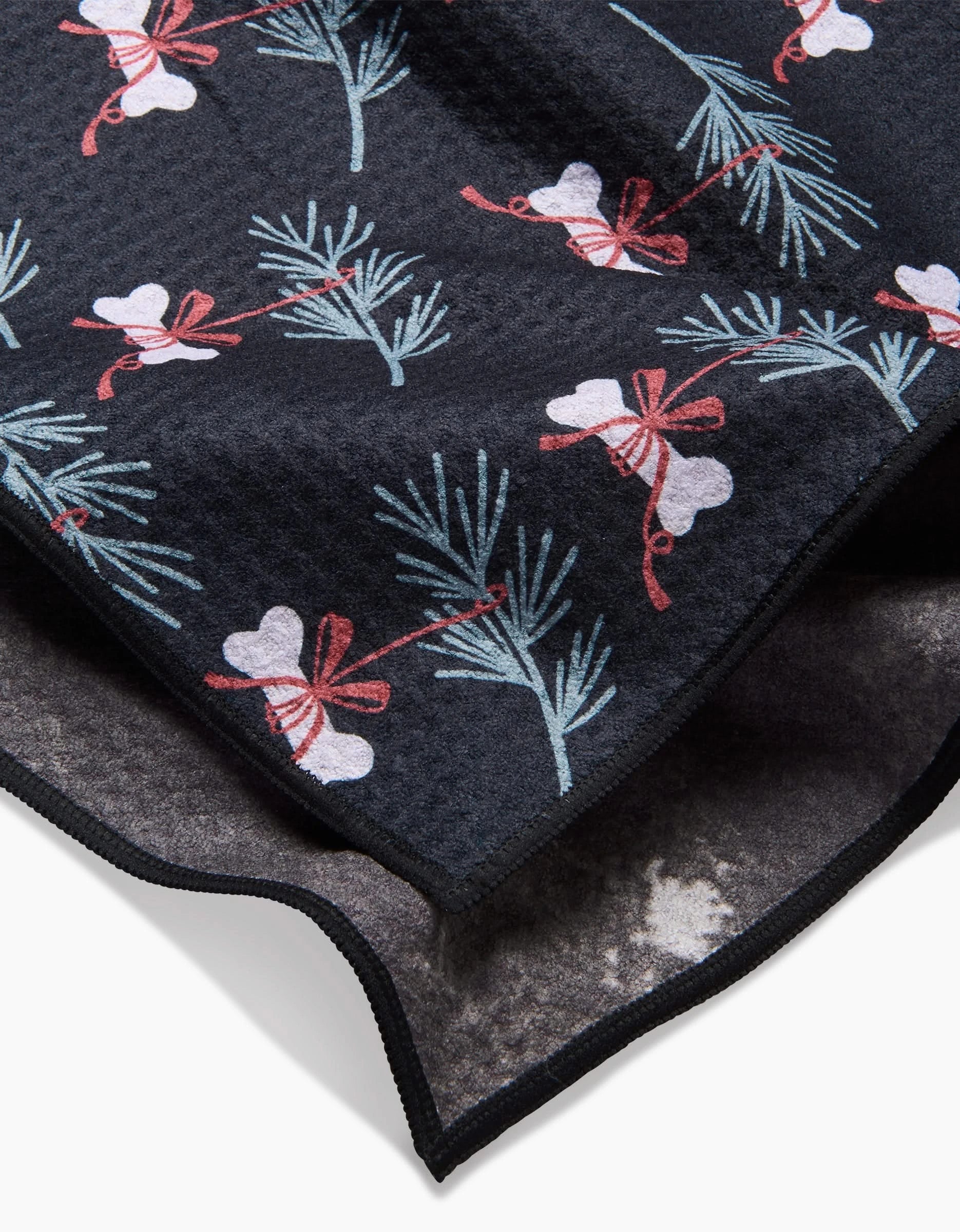 A close-up of the Bones For Christmas recycled PET towel by Charlie Rowan Designs, featuring pine branches and white hearts with red bows, plus a folded edge showing the soft, textured underside.