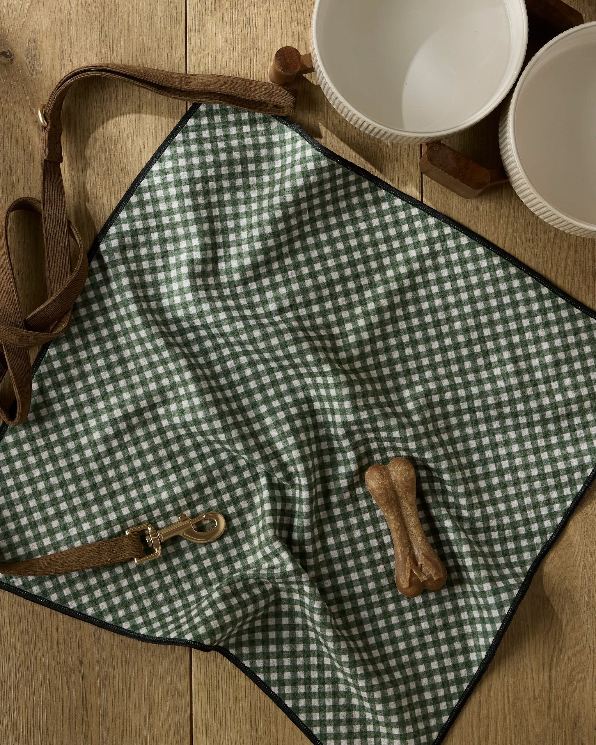 A dog leash and bone sit on a table next to the Geometry Bramble Green ultra-absorbent dog towel—ideal for drying your pup after outdoor fun.