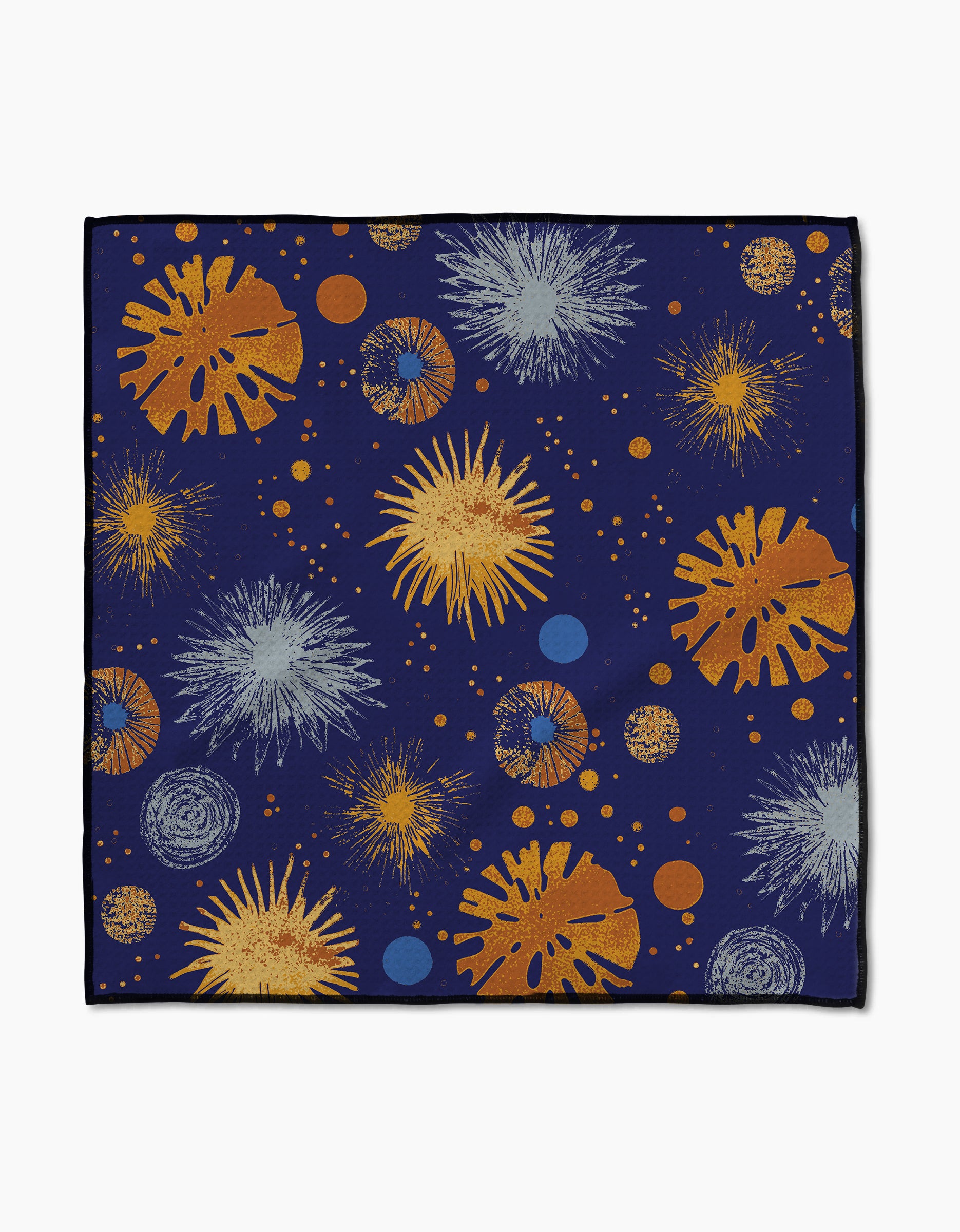 The Bursting Skies Blue Paw Towel by Geometry features a dark blue background with abstract gold, orange, white, and blue fireworks and dots. Made from ultra-absorbent Geoweave fabric with black-edged borders.