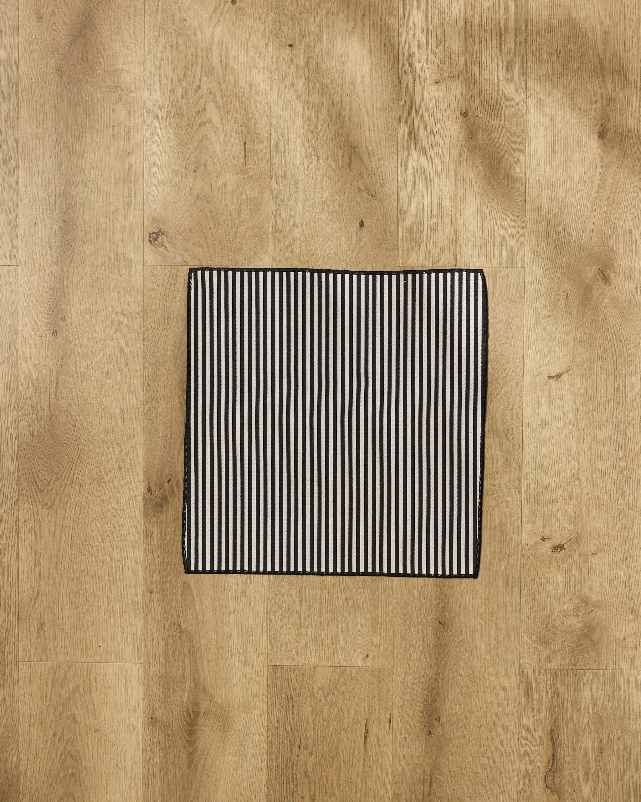 The Geometry Good Pup recycled PET towel, featuring black and white vertical stripes, is displayed on a light wooden floor.