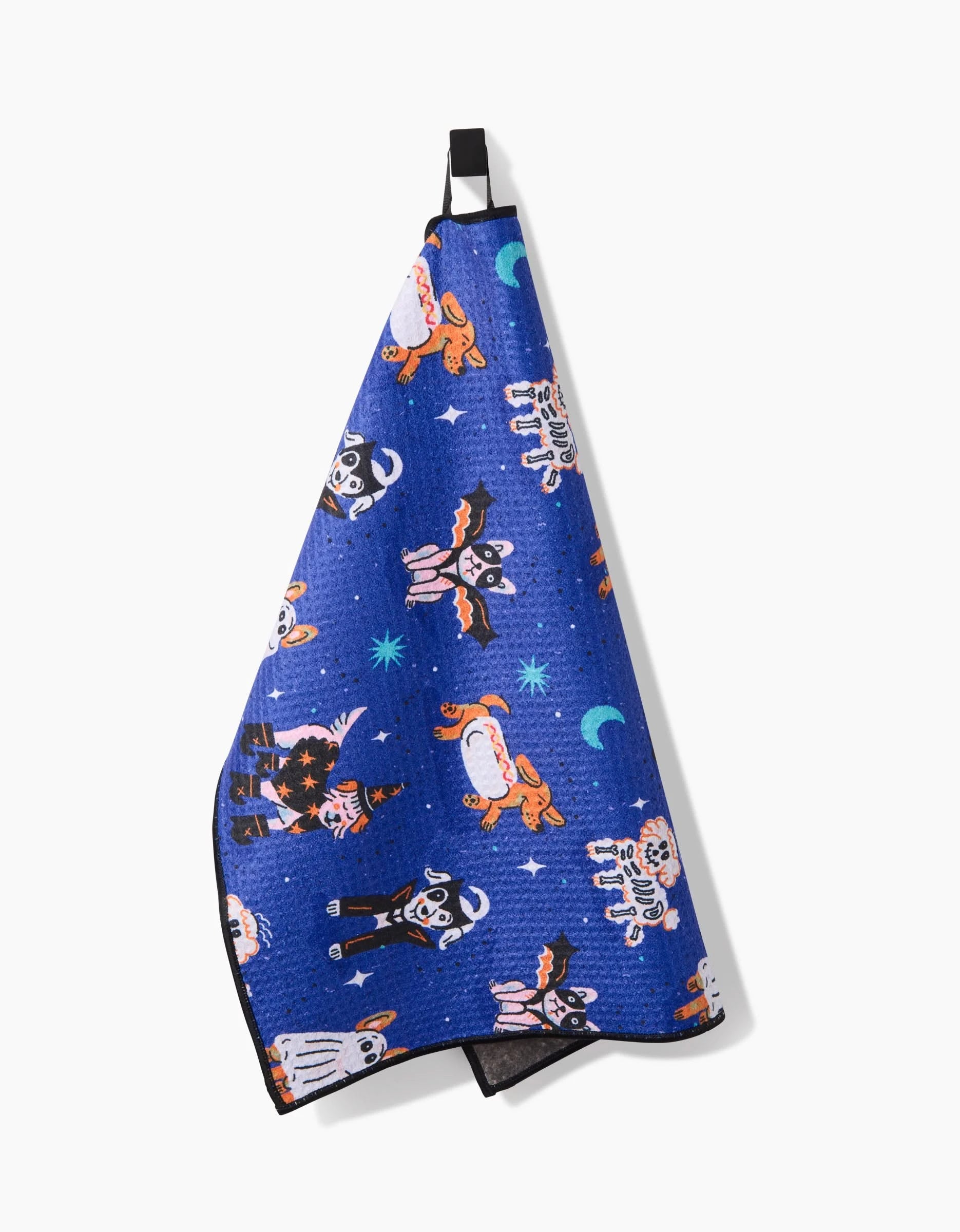 The Halloween Hounds towel by Camila Leão features playful illustrated dogs in space suits with planets, stars, and crescent moons on blue fabric. Ultra-absorbent, it hangs from a black loop against a white background.