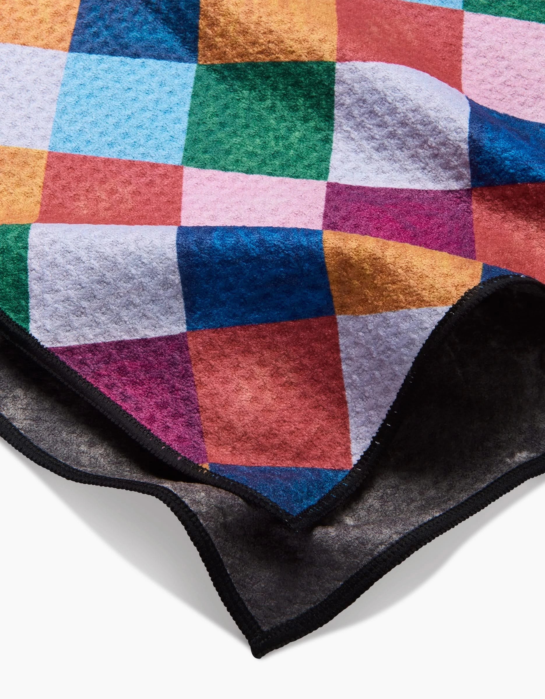 The Daria Solak Holiday Harlequin towel features a soft texture and vibrant checkered pattern with blue, green, red, pink, and orange squares plus black edging, shown draped and folded on a white surface.