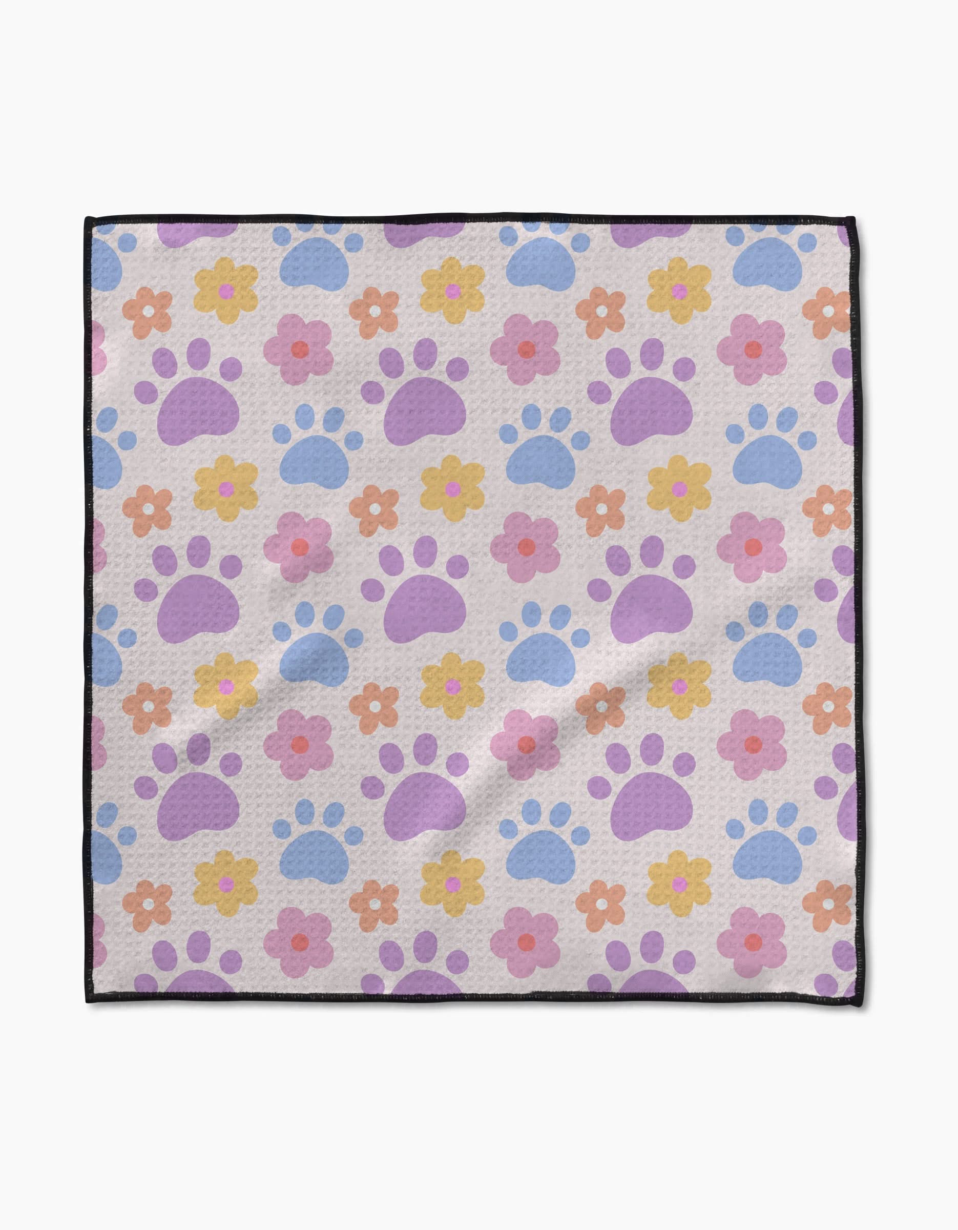 The Paws and Daisies towel by Letters By Shells features pastel blue and purple paw prints with colorful flowers on a light background, black border, and is crafted from ultra-absorbent recycled materials.