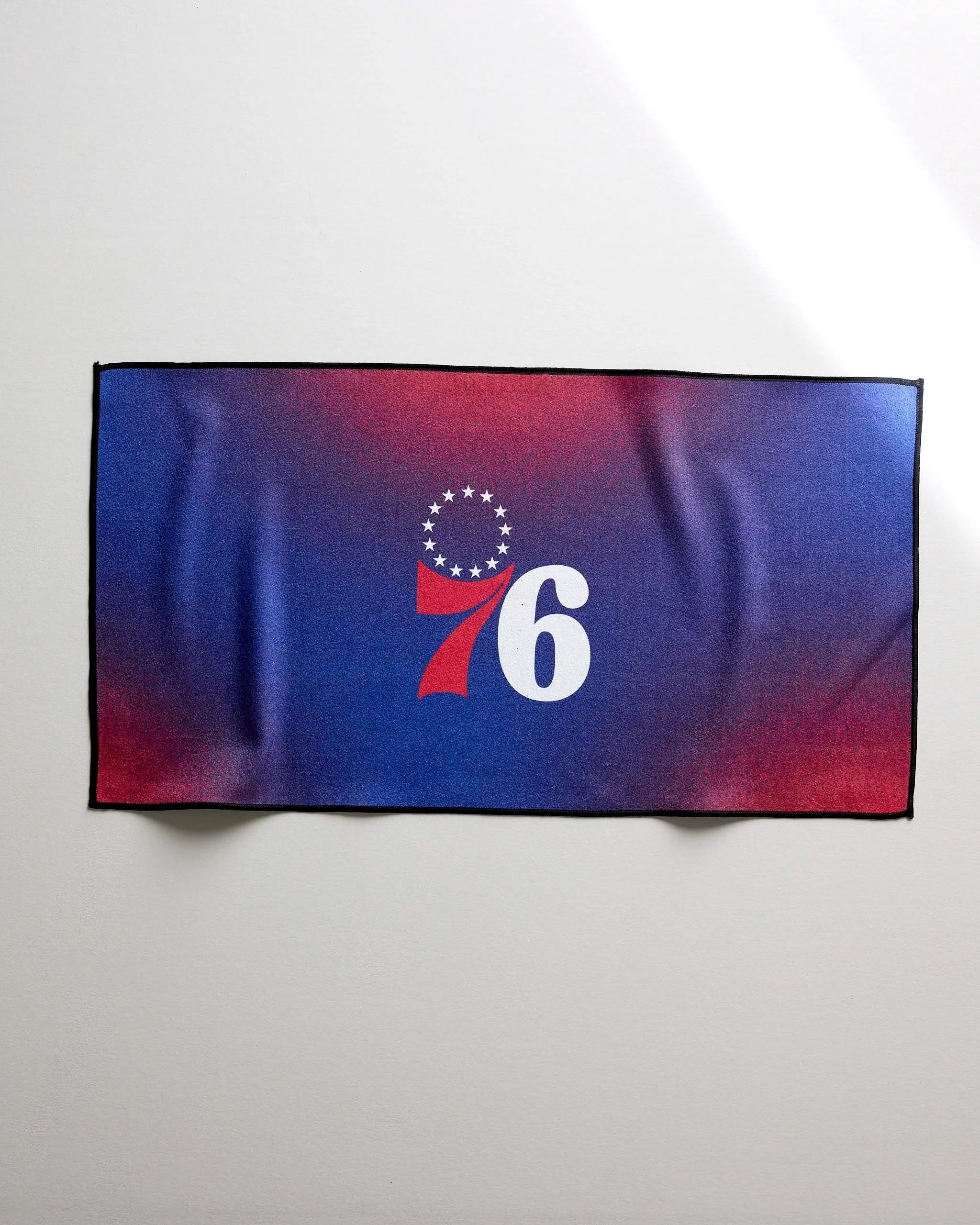 The 76ers Fade by NBALAB x Geometry is a rectangular fitness towel with a blue and red gradient, featuring the number 76 in white and red, plus thirteen white stars forming a semicircle above the 7 at the center.