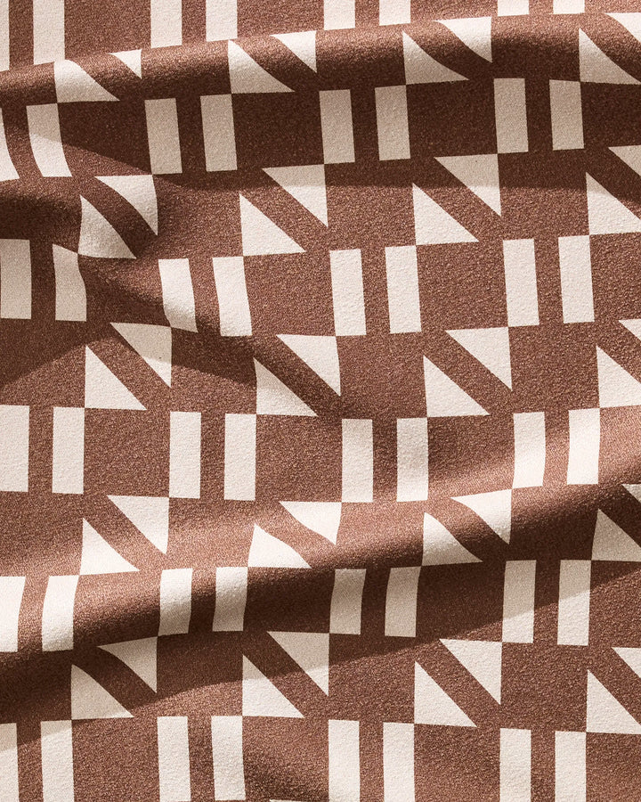 The Affogato fitness towel by Geometry features a modern brown design with white rectangles and triangles in a grid. Ultra-absorbent and slightly wrinkled, it's perfect for workouts.