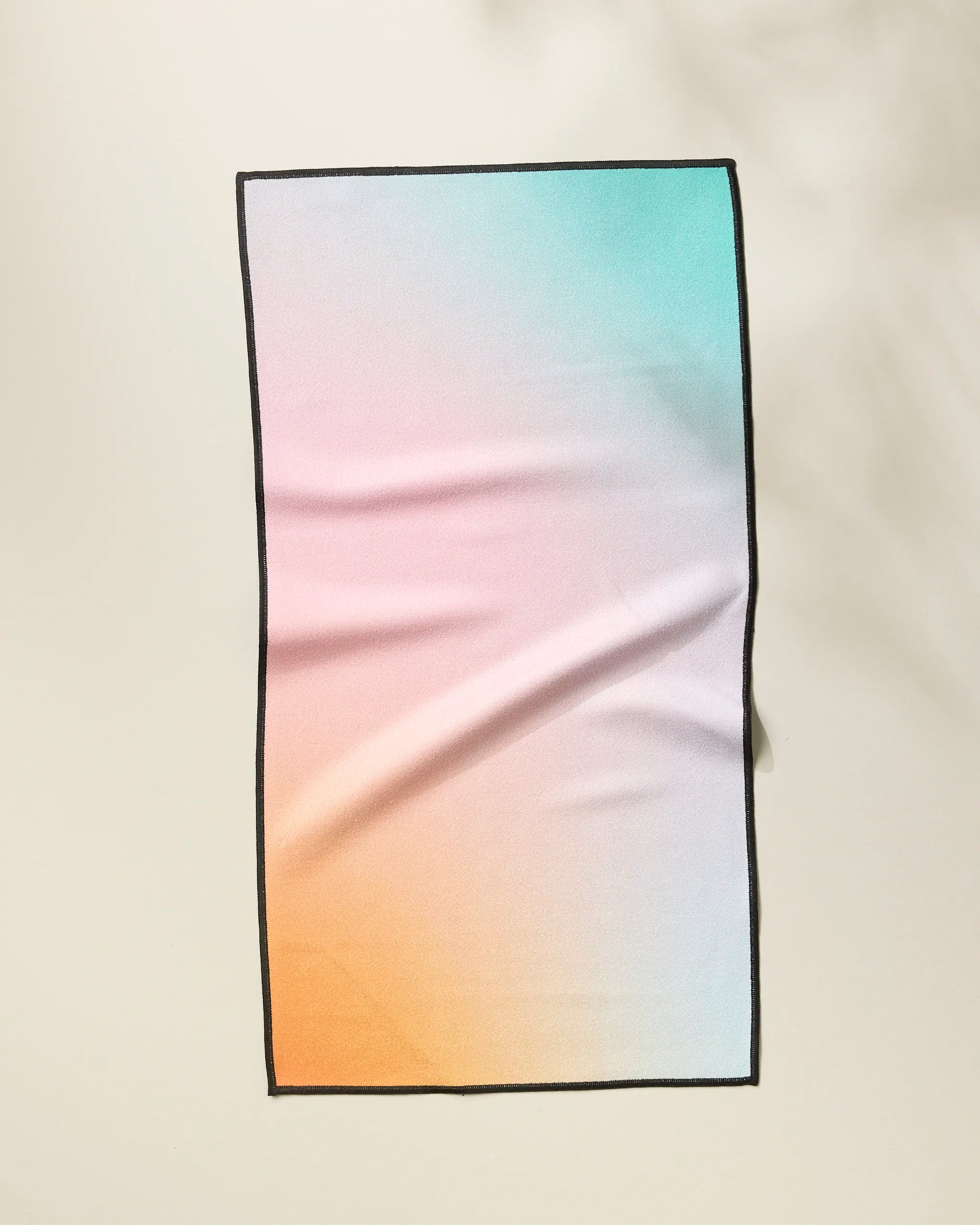 The Geometry Aura Flow fitness towel features a black border and a smooth gradient from turquoise to pastel pink and orange. Ultra-absorbent and fast-drying, it’s perfect for post-workout use. Shown flat with slight creases on a light surface.