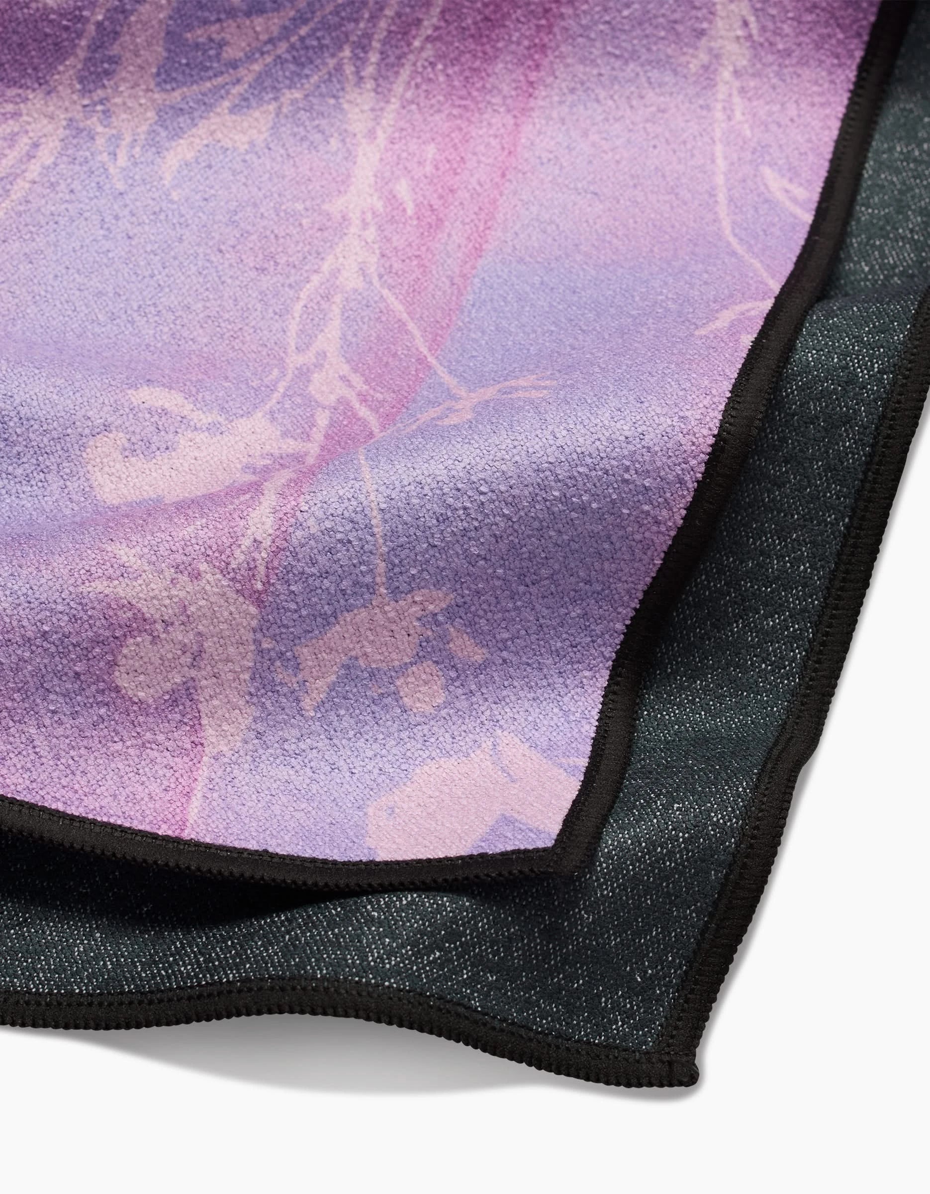 A close-up of GEOMETRY’s Bloom Blend shows two recycled fabric layers: the top is soft, light purple with a subtle botanical print; the bottom is dark and textured. Both have black stitched edges.