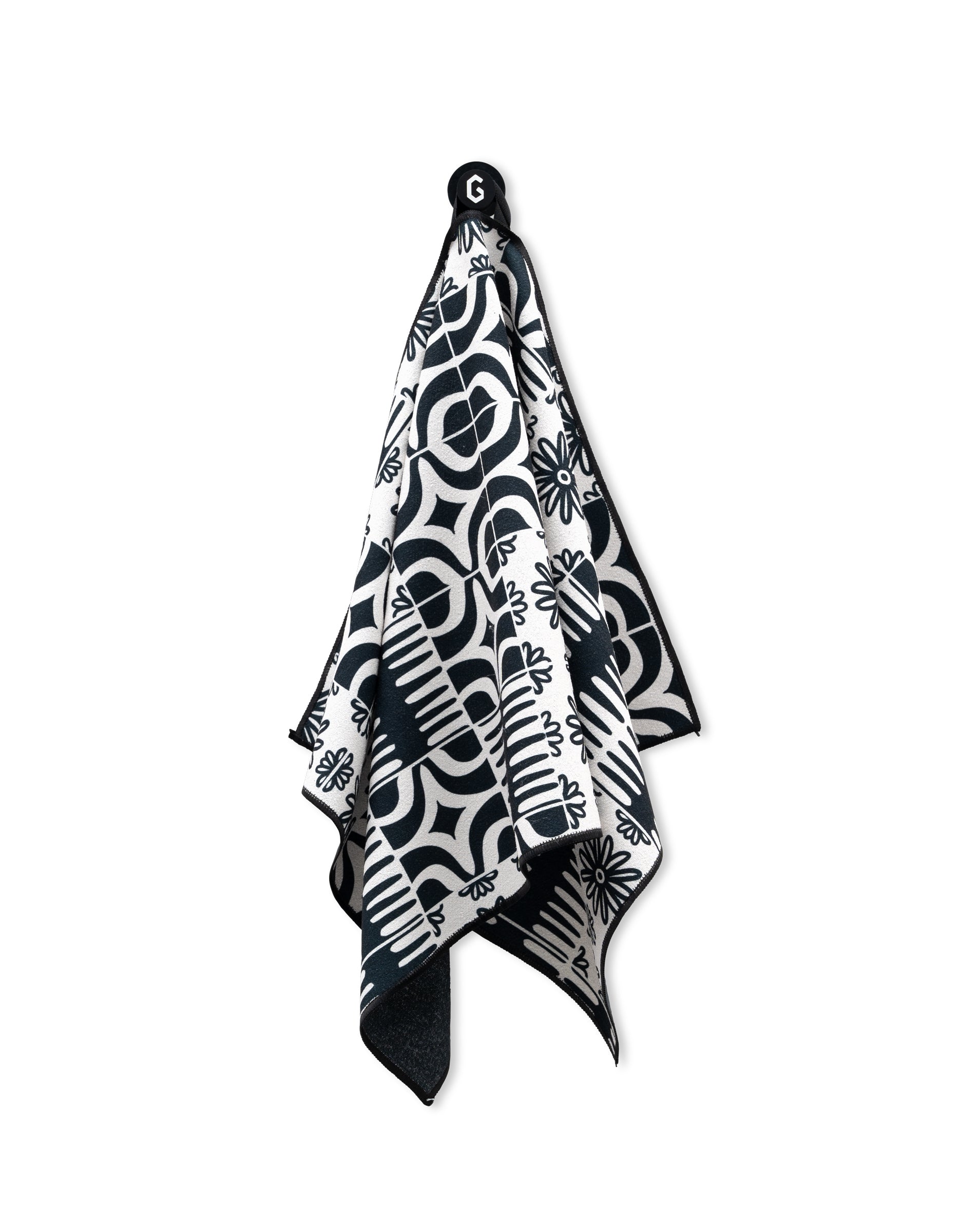 The GEOMETRY Magna - Bohemian Mosaic is a black and white ultra-absorbent gym towel featuring bold geometric and floral patterns, hanging by a black loop.
