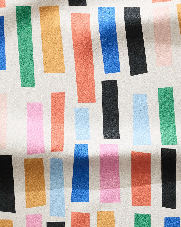 A vibrant white fitness towel by Jennifer Bouron, named Bricks, features ultra-absorbent, quick-drying rectangles in green, orange, pink, blue, black, and red scattered across the surface.
