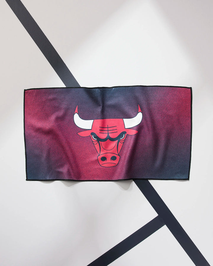 The NBALAB x Geometry Bulls Fade is a sustainable gym towel with the Chicago Bulls logo and a red-black gradient, displayed on a wall with diagonal black lines—ideal for NBA fitness towel fans.