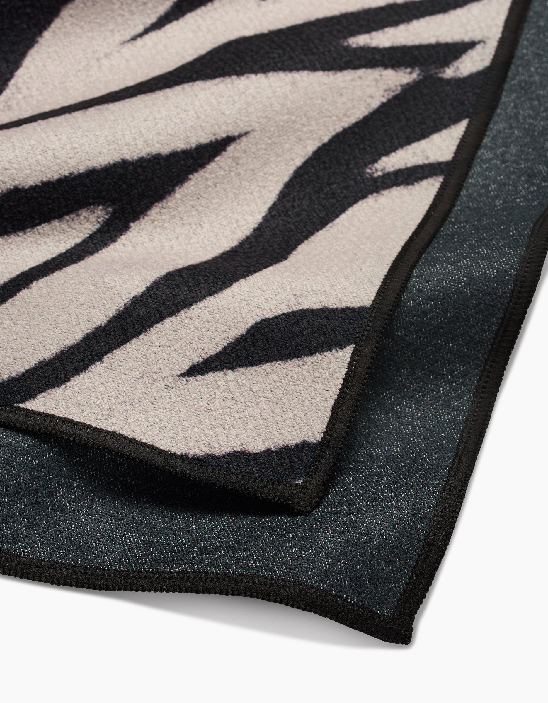 A close-up of the GEOMETRY Chase Fitness Towel, featuring a soft beige and black zebra print with black trim, crafted from recycled materials and displayed on a dark fabric surface.