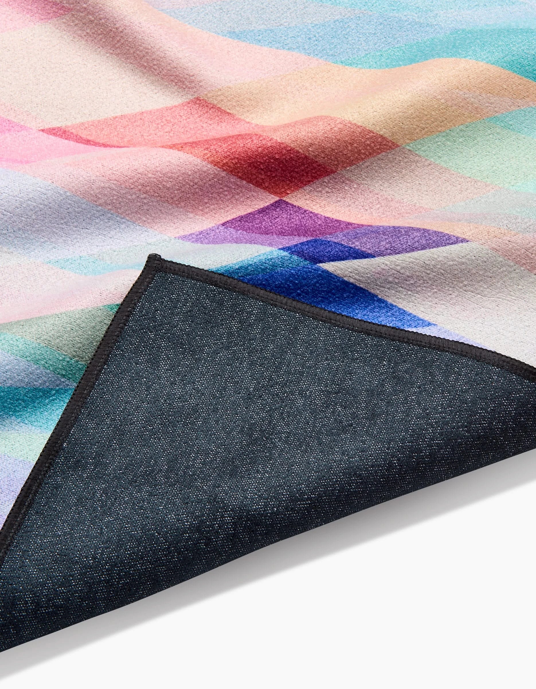 The Rachel Parker Eventide blanket showcases colorful geometric patterns made from recycled materials, featuring pastel shades on one side and dark, textured fabric on the reverse, partially folded to display both sides.