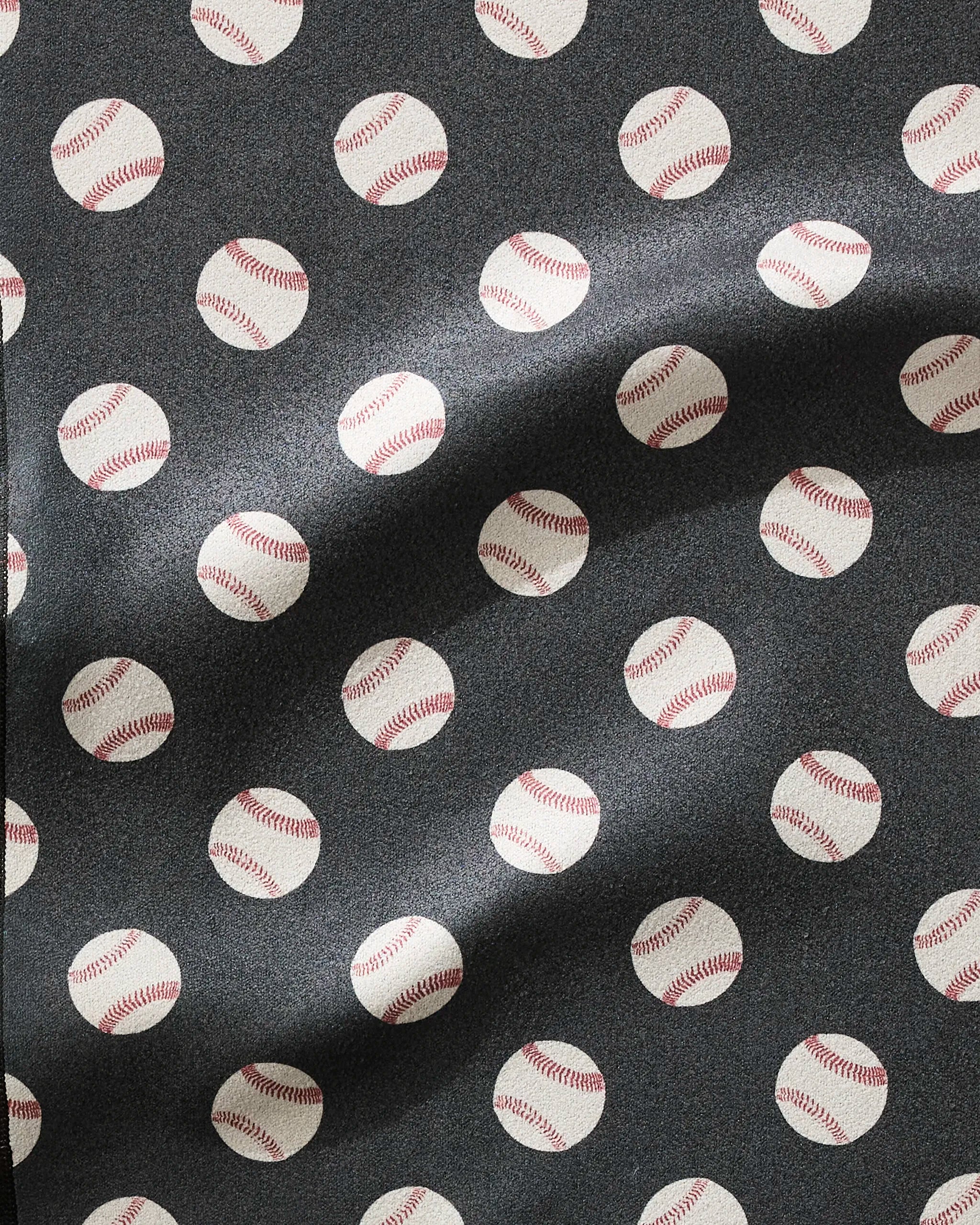 A close-up of the Geometry Fastball fitness towel shows ultra-absorbent fabric with a repeating white baseball pattern on dark background. Waves in the towel highlight its fast-drying properties and soft texture.