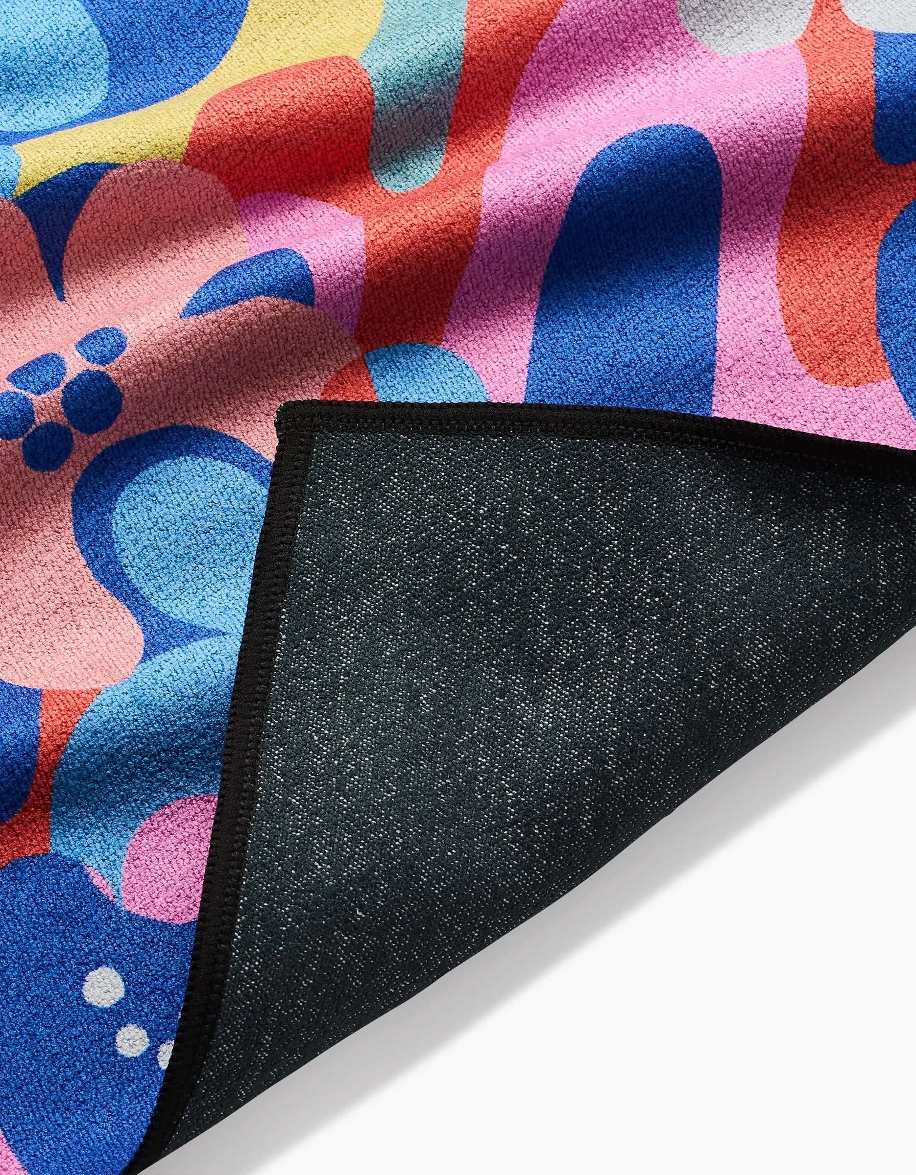 A close-up of Flower Powers by Masha Volnova shows a vivid, abstract textile in red, blue, pink, yellow, and white curves. Made from recycled materials, it features a folded corner revealing its dark textured backing.