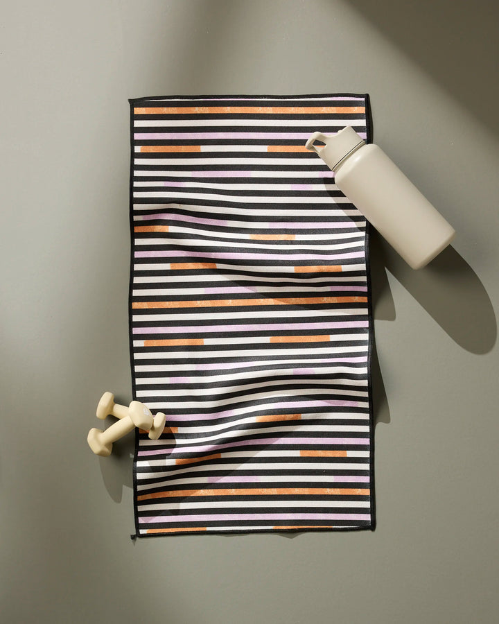 A cream Funk On water bottle and two small cream dumbbells sit on Geometry's ultra-absorbent towel with black, white, and brown stripes, all arranged on a light gray surface with soft shadows.