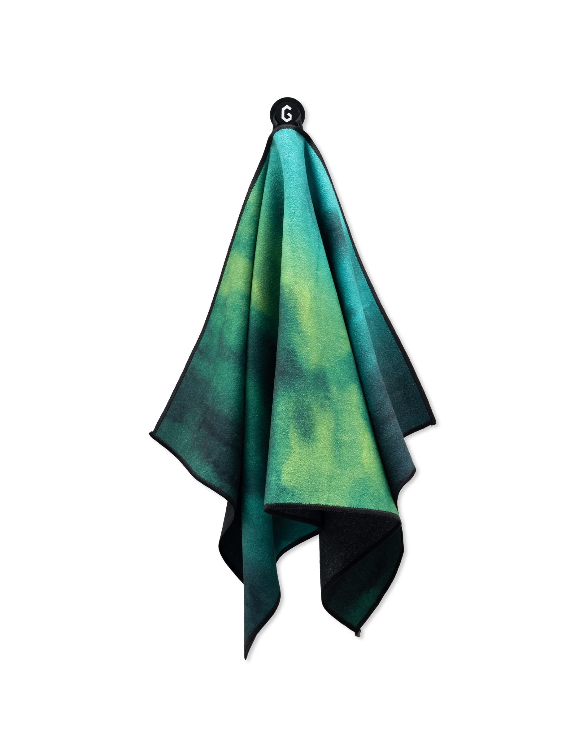 The GEOMETRY Magna - Greens is a green and blue tie-dye golf towel made from recycled materials, hanging from a black G-logo hook, shown against a white background.