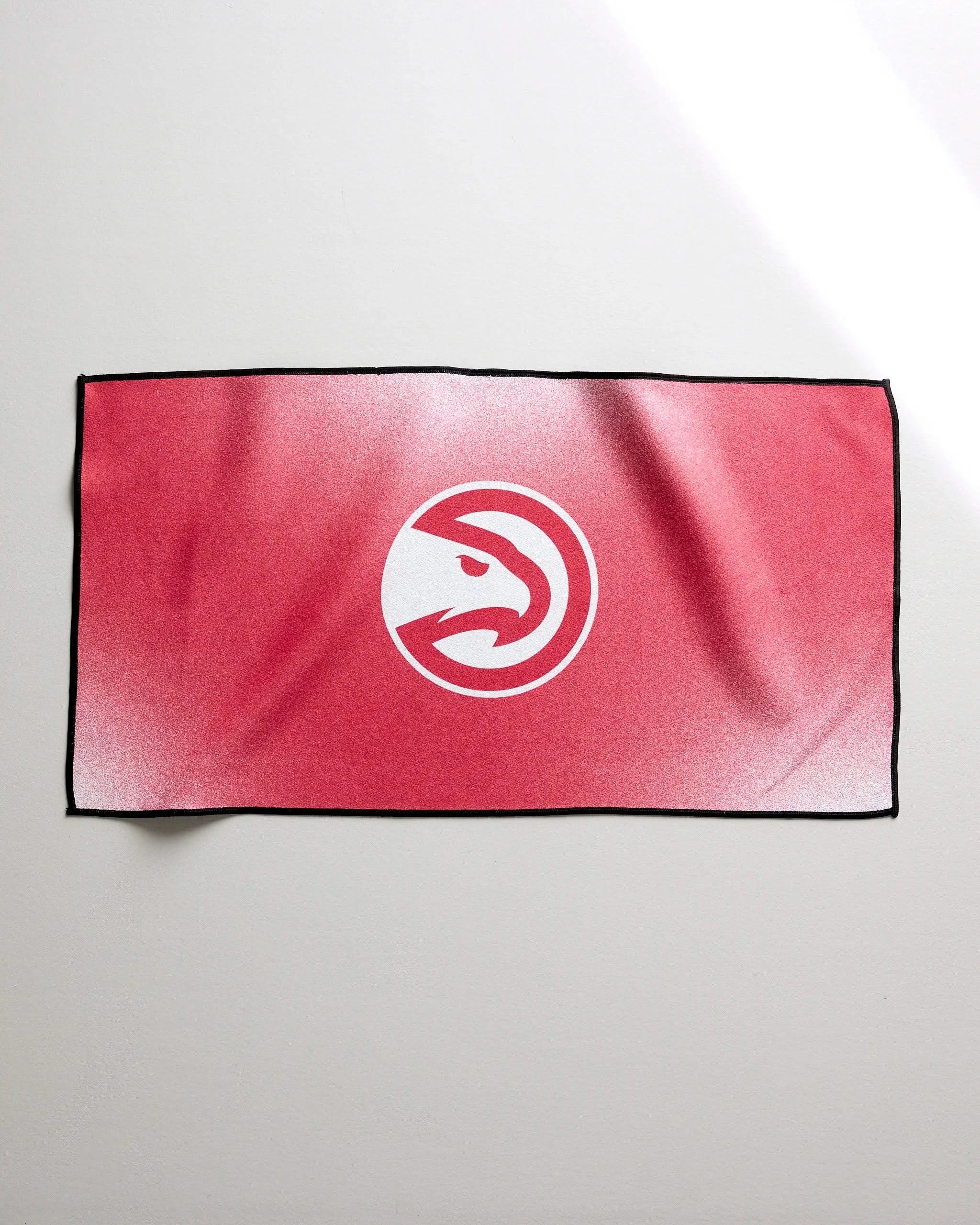 The Hawks Fade towel by NBALAB x Geometry is a rectangular red fitness towel with a white Atlanta Hawks logo at the center—ideal as a quick-drying gym accessory for basketball fans.
