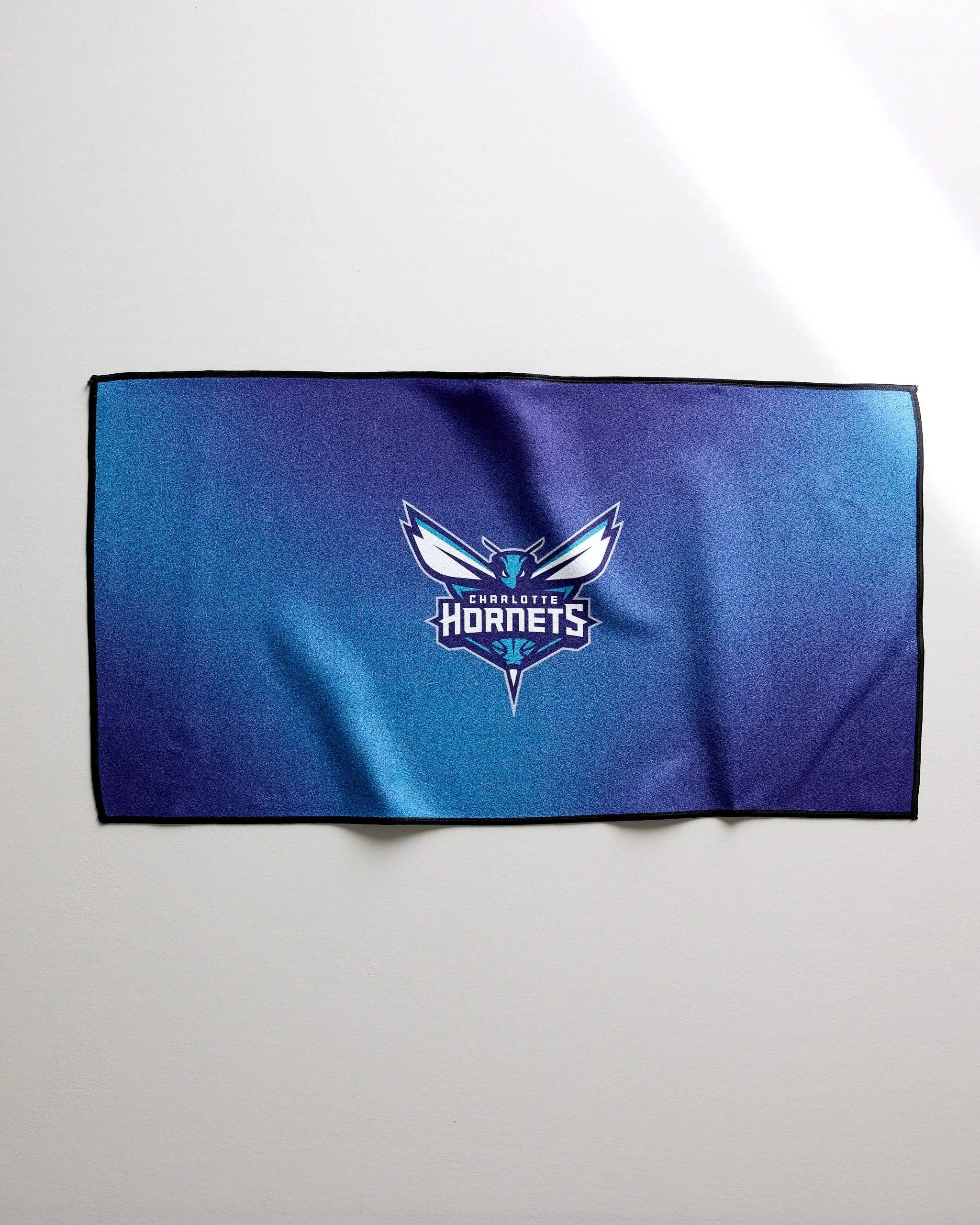 The Hornets Fade towel by NBALAB x Geometry is a blue and purple NBA fitness towel with the Charlotte Hornets logo and name centered, displayed flat on a light surface.