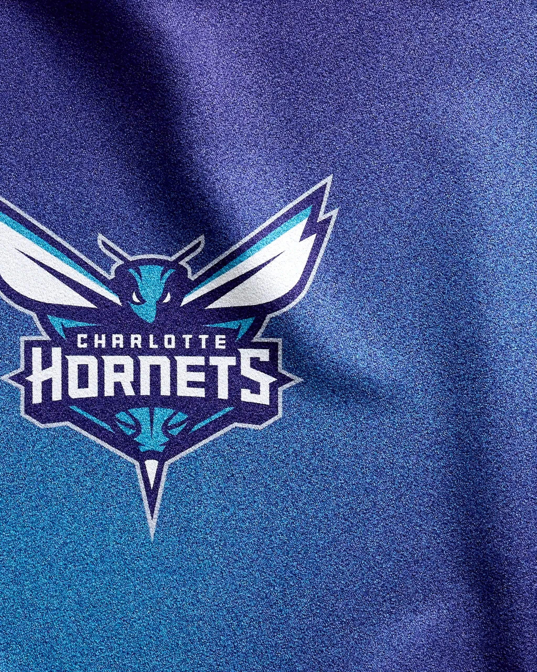 The image displays the Hornets Fade by NBALAB x Geometry, featuring the Charlotte Hornets logo on a blue and purple textured background—a quick-drying gym towel that's both stylish and functional for NBA fans.