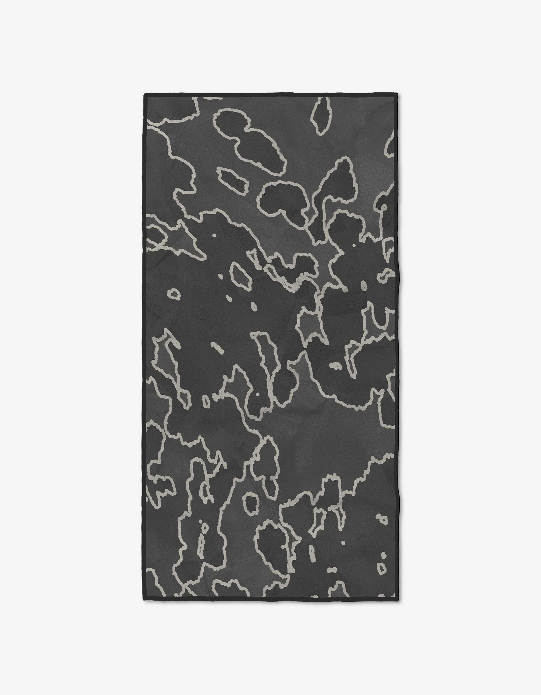 The GEOMETRY Iron and Ink mat is rectangular, black, and crafted from recycled materials. It features an abstract pattern of irregular light-gray outlines resembling contour lines or organic shapes, shown on a white background.