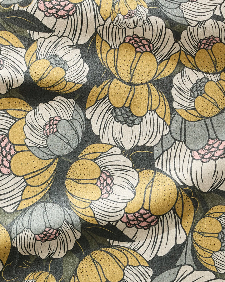 A close-up of Lakeside Bloom by Ash Cascade, an ultra-absorbent towel with a dark background and large yellow, white, gray, and pink stylized floral pattern. The slightly wrinkled surface adds depth and texture.
