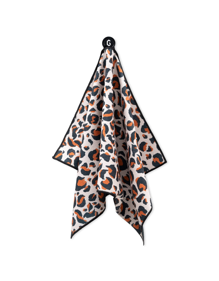 The GEOMETRY Magna - Leopard fitness towel features a brown, black, and white leopard print with black edging. Ultra-absorbent and soft, it hangs from a hook in gentle folds.