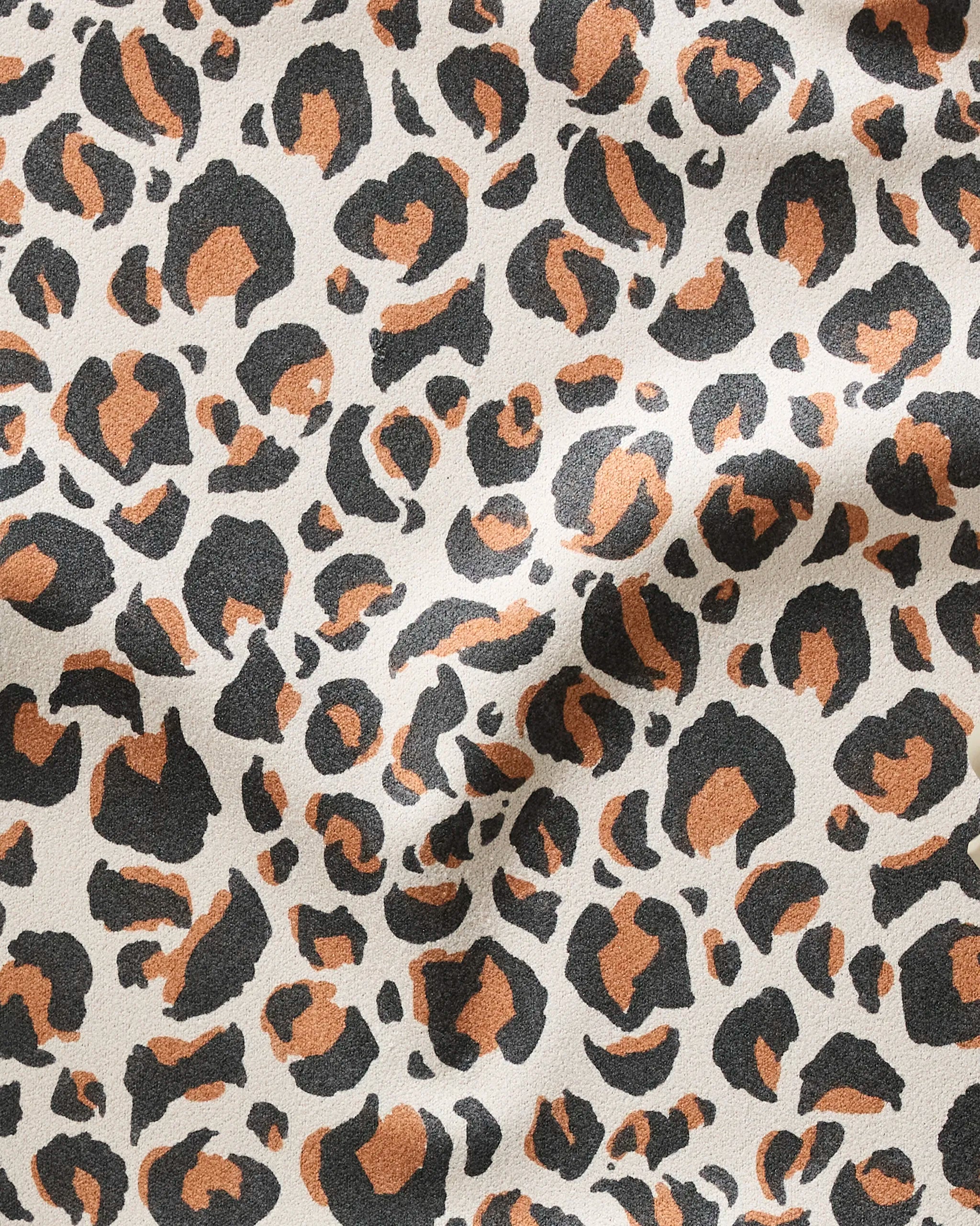 A close-up of the GEOMETRY 'Leopard' fitness towel, crafted from recycled materials, displays its beige fabric with black and brown leopard spots, visible textured folds, and ultra-absorbent quality.