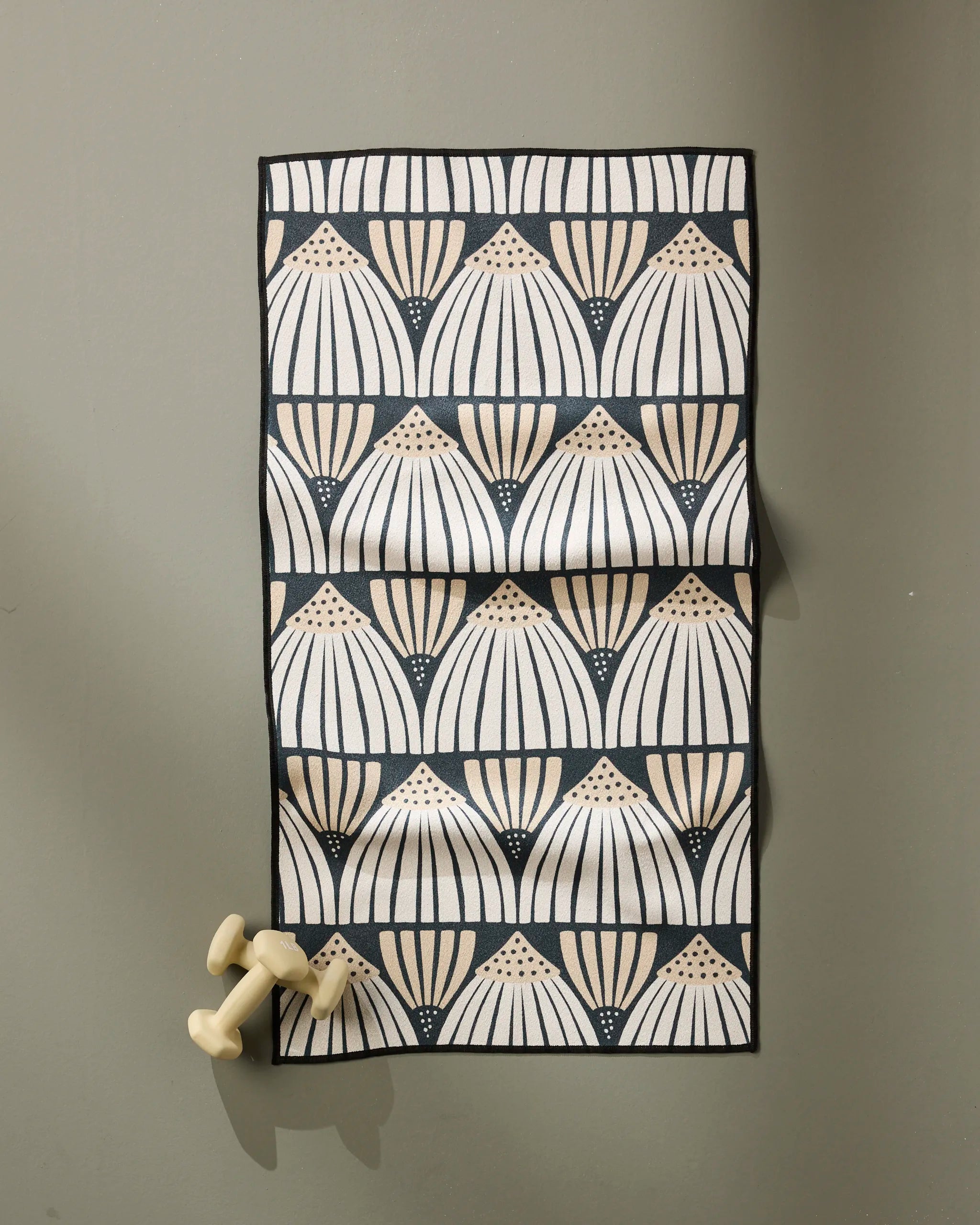 The Amy MacCready Letitia is a rectangular, ultra-absorbent mat featuring a cream and tan geometric fan pattern on black, shown on gray with two small cream weights in the corner.