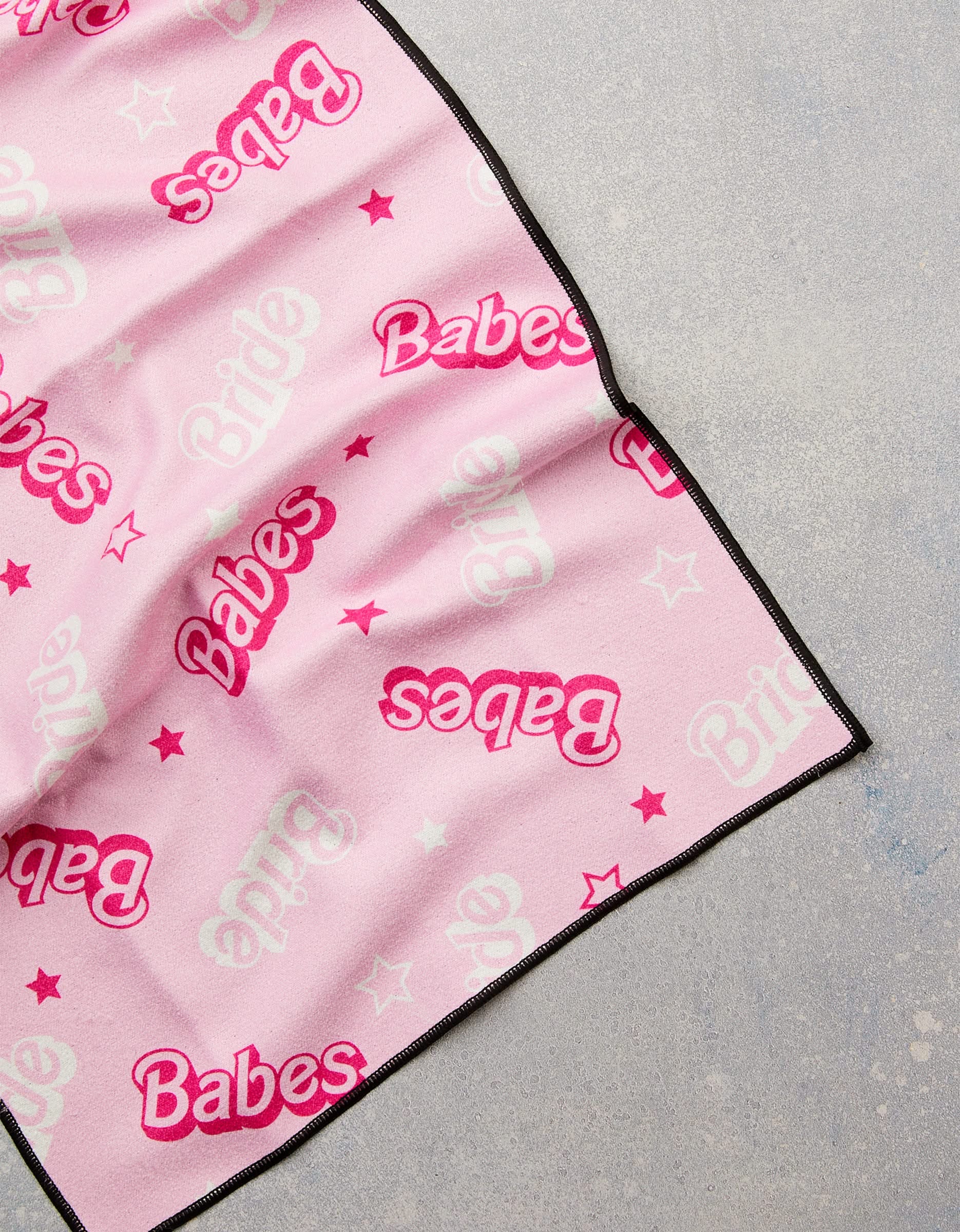 The GEOMETRY Lets Go Party towel is a pink fitness towel with black trim, red Babes and white Bride text, star designs, and is ultra-absorbent—crafted from post-consumer recycled materials. Shown laid on a light gray surface.