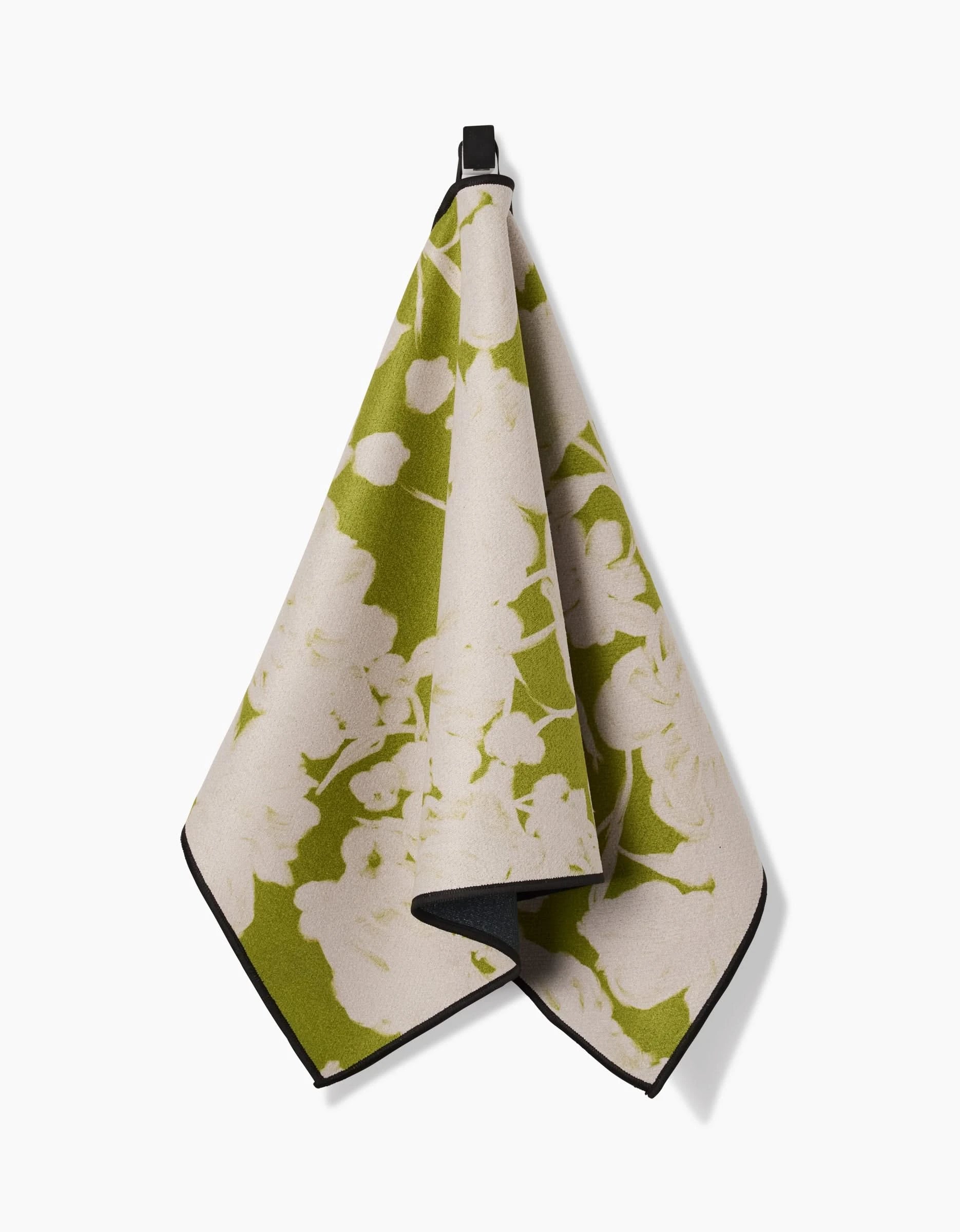 The GEOMETRY Meadow Mist fitness towel, featuring a green and cream floral design and made from recycled materials, hangs by a small black loop against a plain white background.