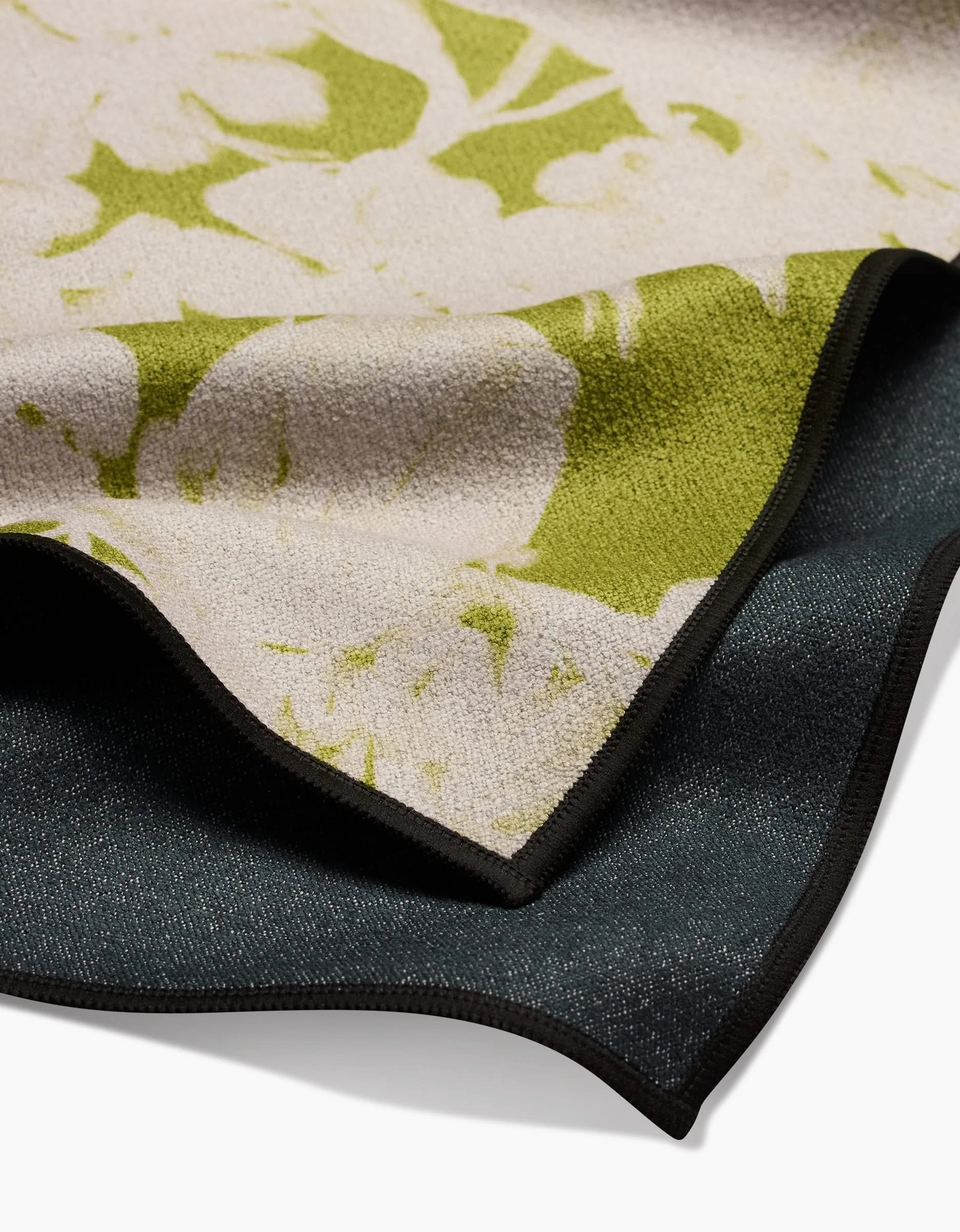 A close-up of GEOMETRY’s Meadow Mist shows layered recycled fabric: light beige and green floral on top, dark textured material beneath, both finished with black stitching.
