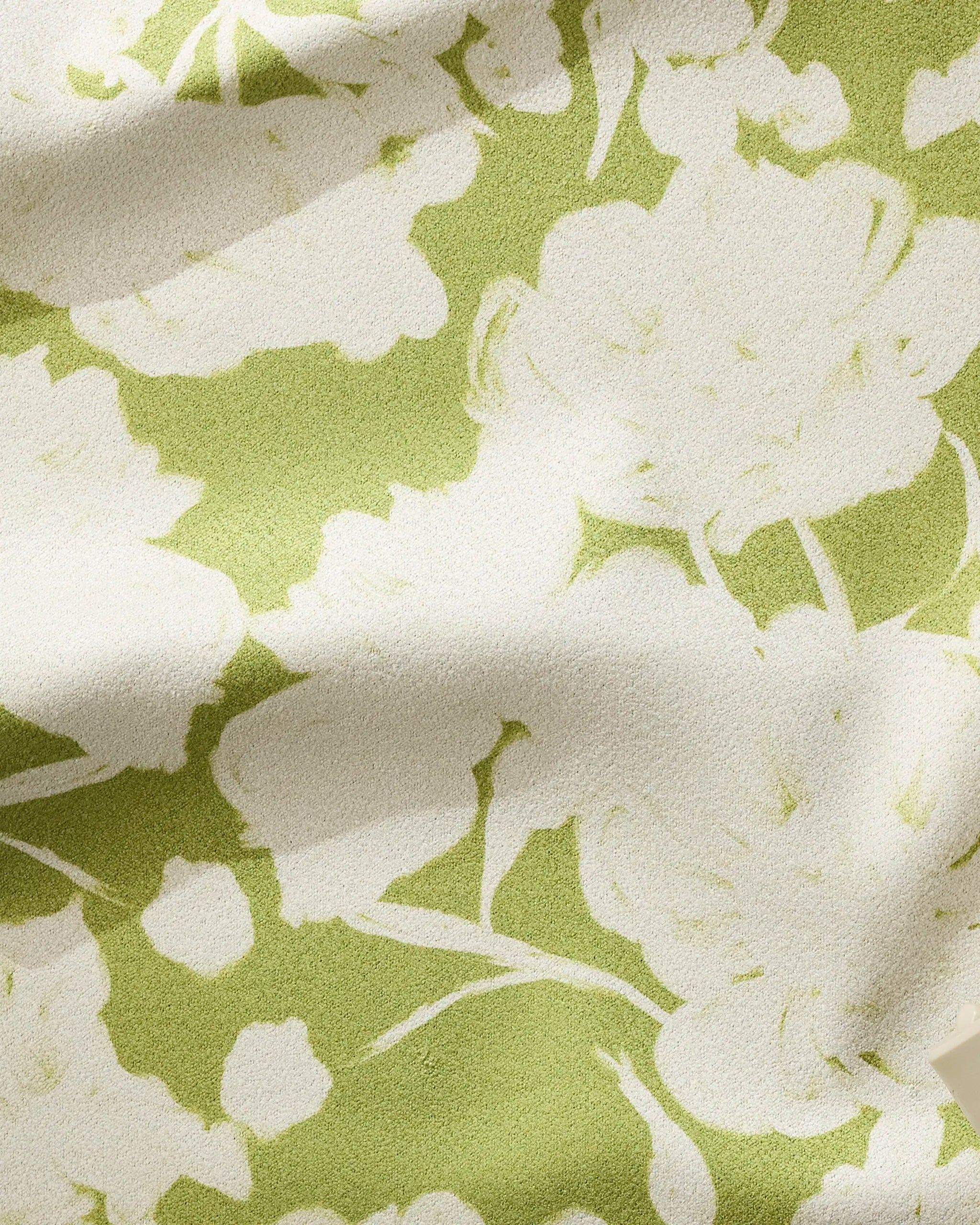 A close-up of Meadow Mist by GEOMETRY: light green fabric with a white floral pattern, soft folds, and textured surface—perfect as a fast-drying, ultra-absorbent fitness towel.
