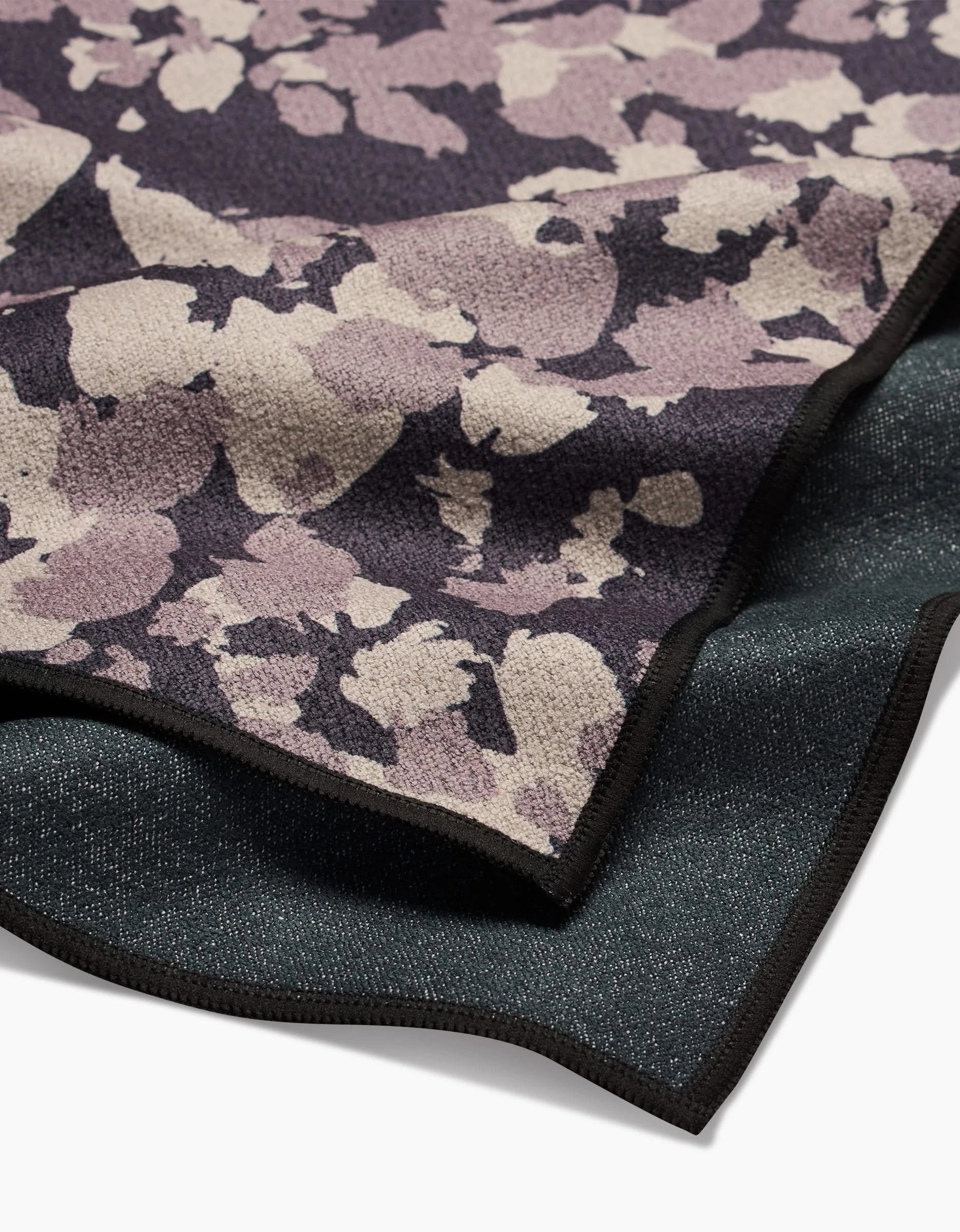 A close-up of two overlapping GEOMETRY Metro Mesh fabric swatches, one with a purple and beige abstract floral pattern, the other a dark ultra-absorbent solid—both featuring black finished edges and made from recycled materials.