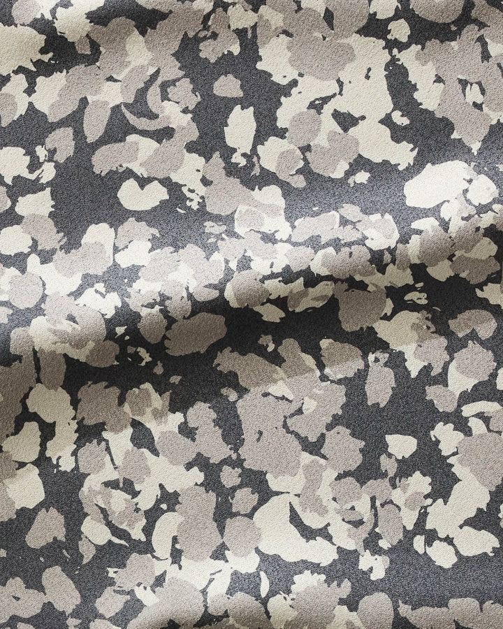 A close-up of GEOMETRY’s Metro Mesh fabric, crafted from recycled materials, shows gentle folds and texture with a light beige and gray abstract spotted pattern on a dark background.