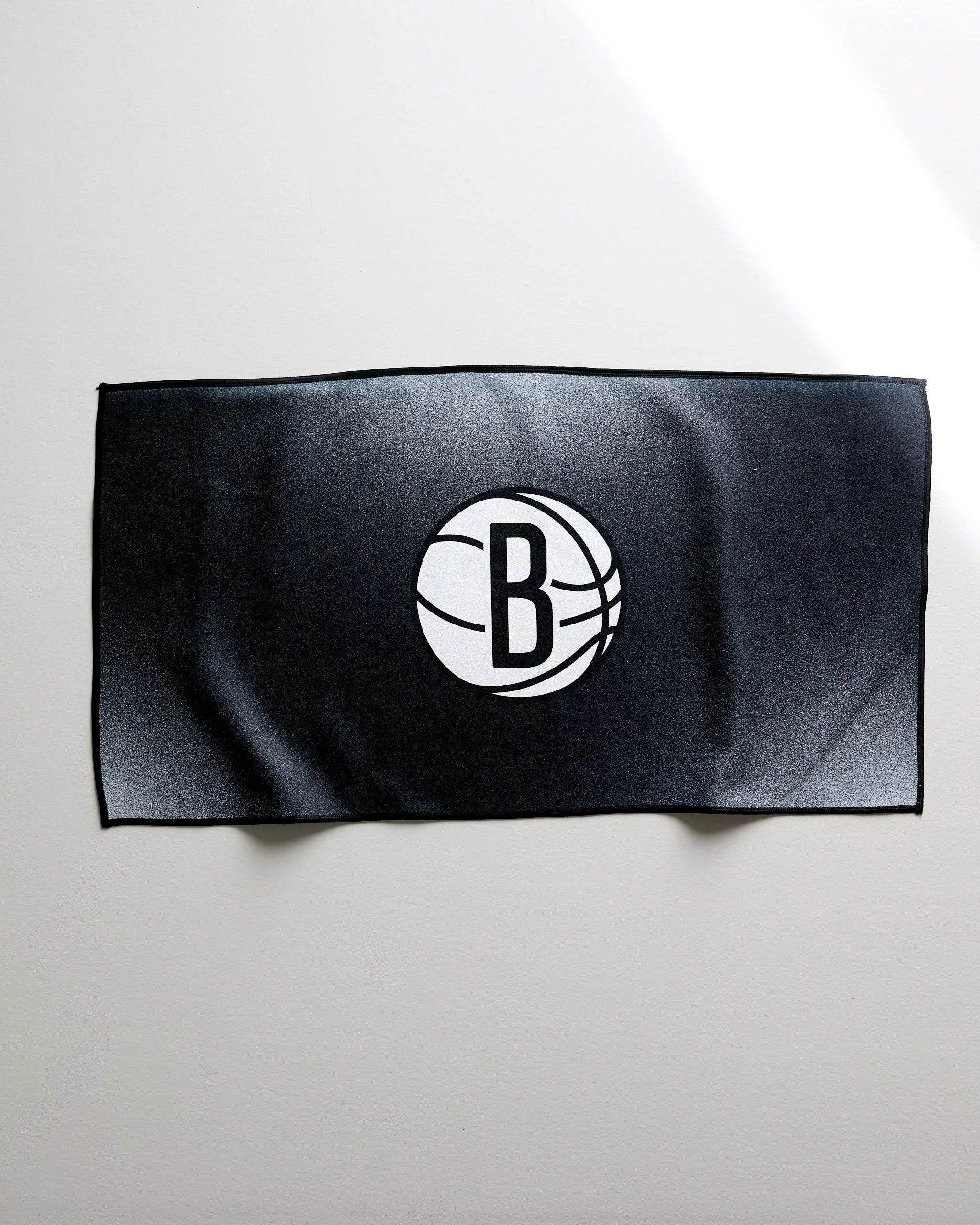The NBALAB x Geometry Nets Fade towel is a black, rectangular, quick-drying gym towel featuring the Brooklyn Nets logo—a white basketball with a B—set against a plain light background.