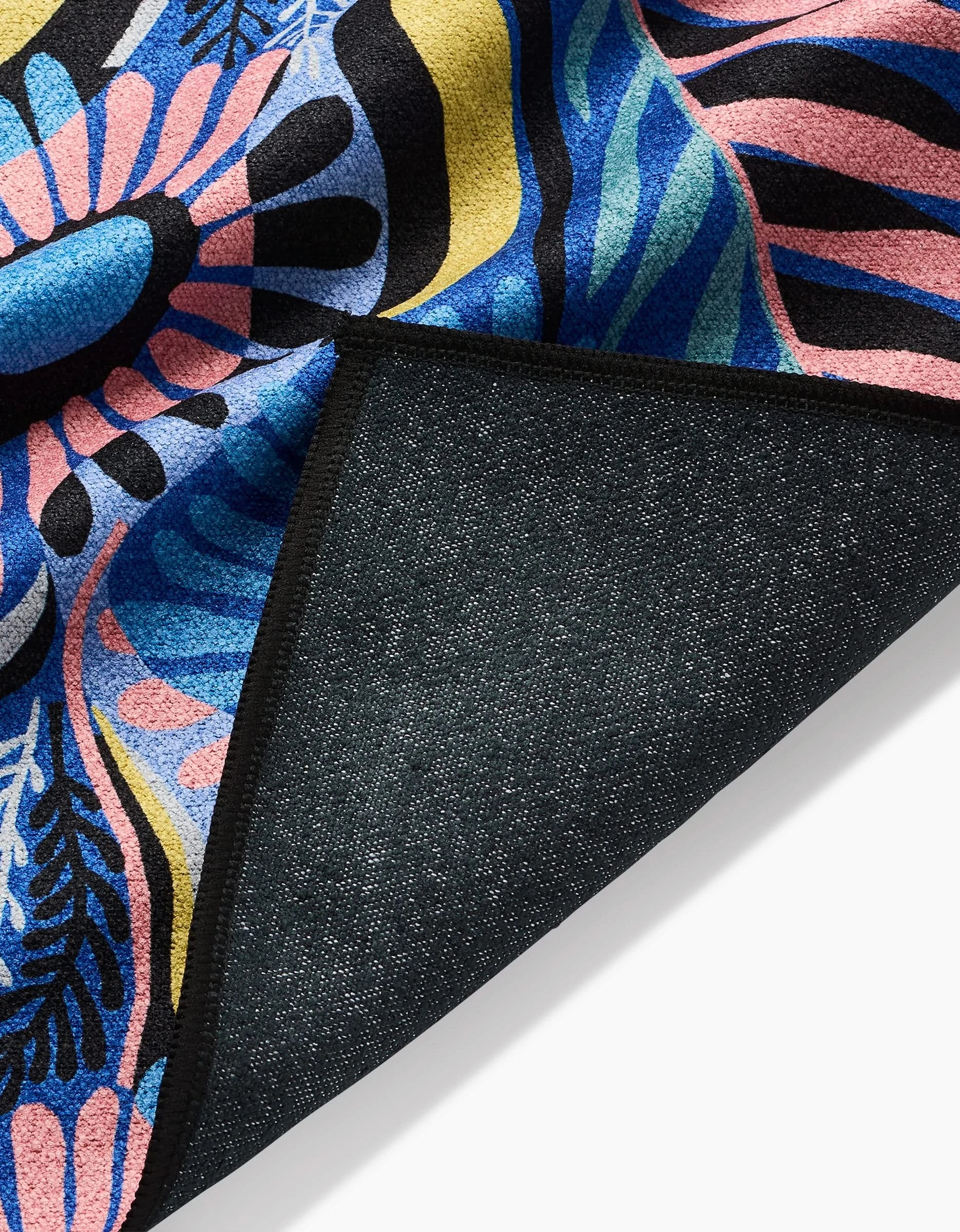A close-up of the Palm Beach fitness towel by Masha Volnova, featuring a colorful abstract pattern with blue, pink, yellow, and black shapes on ultra-absorbent recycled fabric. The folded edge reveals textured stitching underneath.