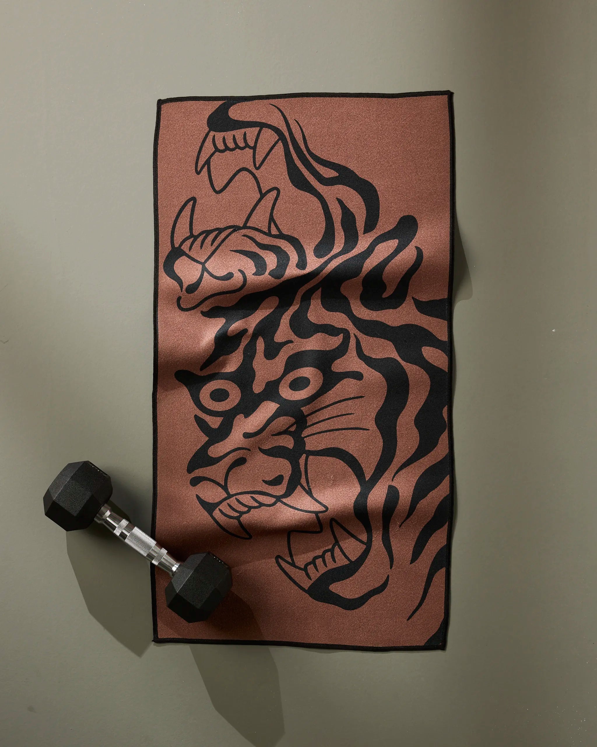 A Cole Strem "Panther In Brown" fitness towel with a striking black panther face design rests on a gray surface, topped by a black dumbbell.