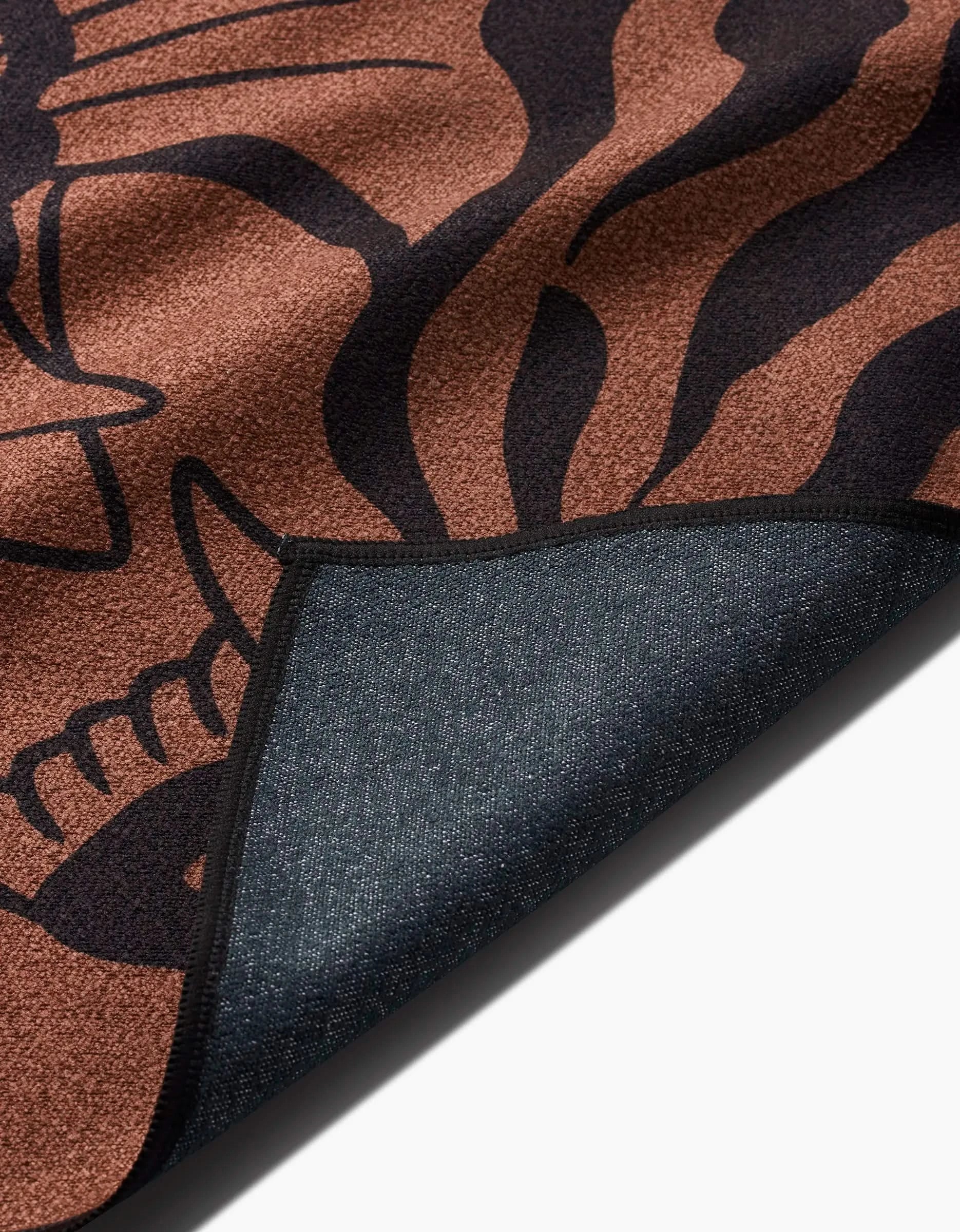 A close-up of Cole Strems Panther In Brown rug, featuring a black abstract pattern on recycled material, with a dark textured backing, partially folded to showcase both sides.