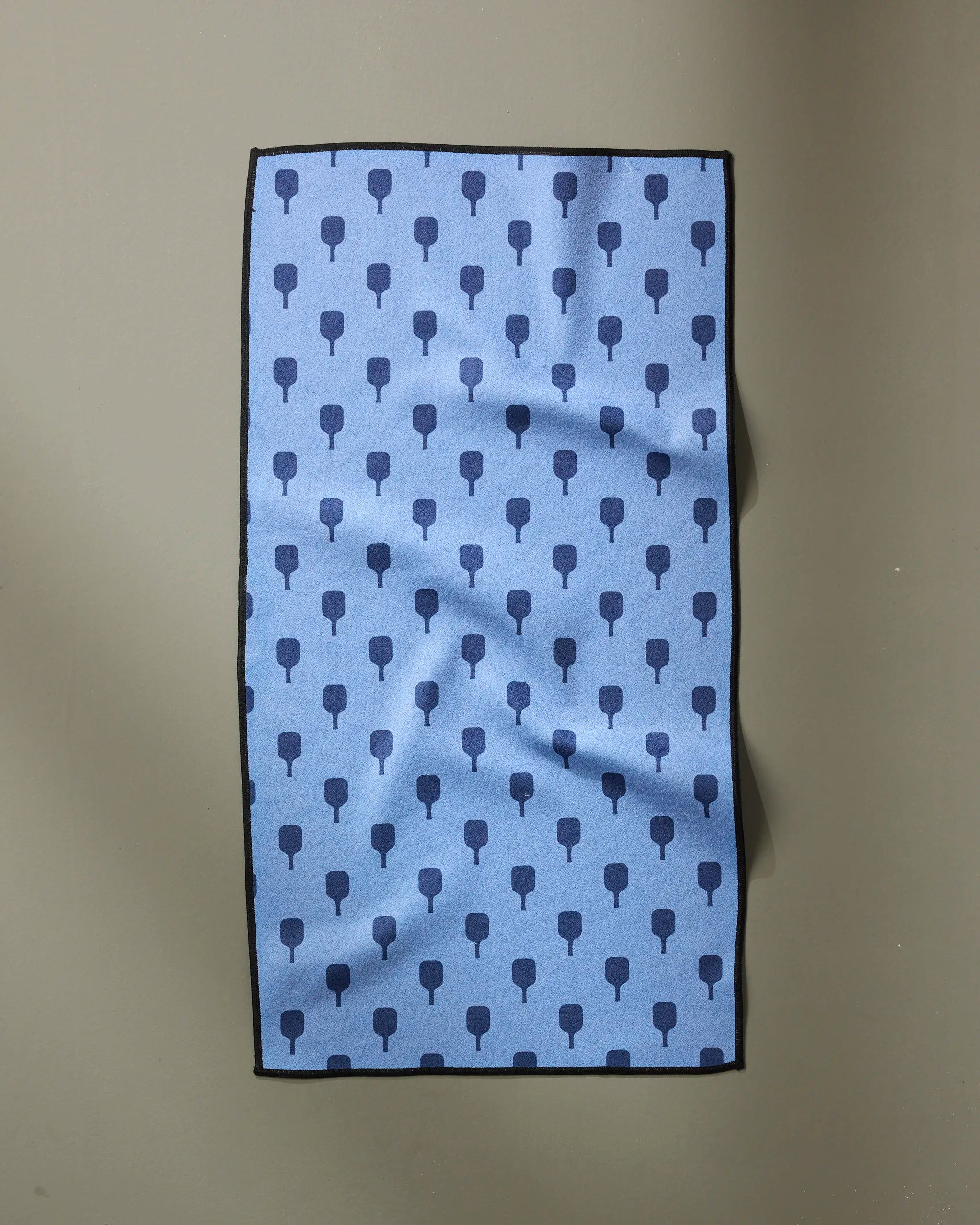 The Modern Dad’s “Pickle Ball Anyone” is a rectangular blue fitness towel with a dark blue tree-like pattern, black edges, and slight wrinkles. Ultra-absorbent for quick drying after workouts; shown on a plain gray background.