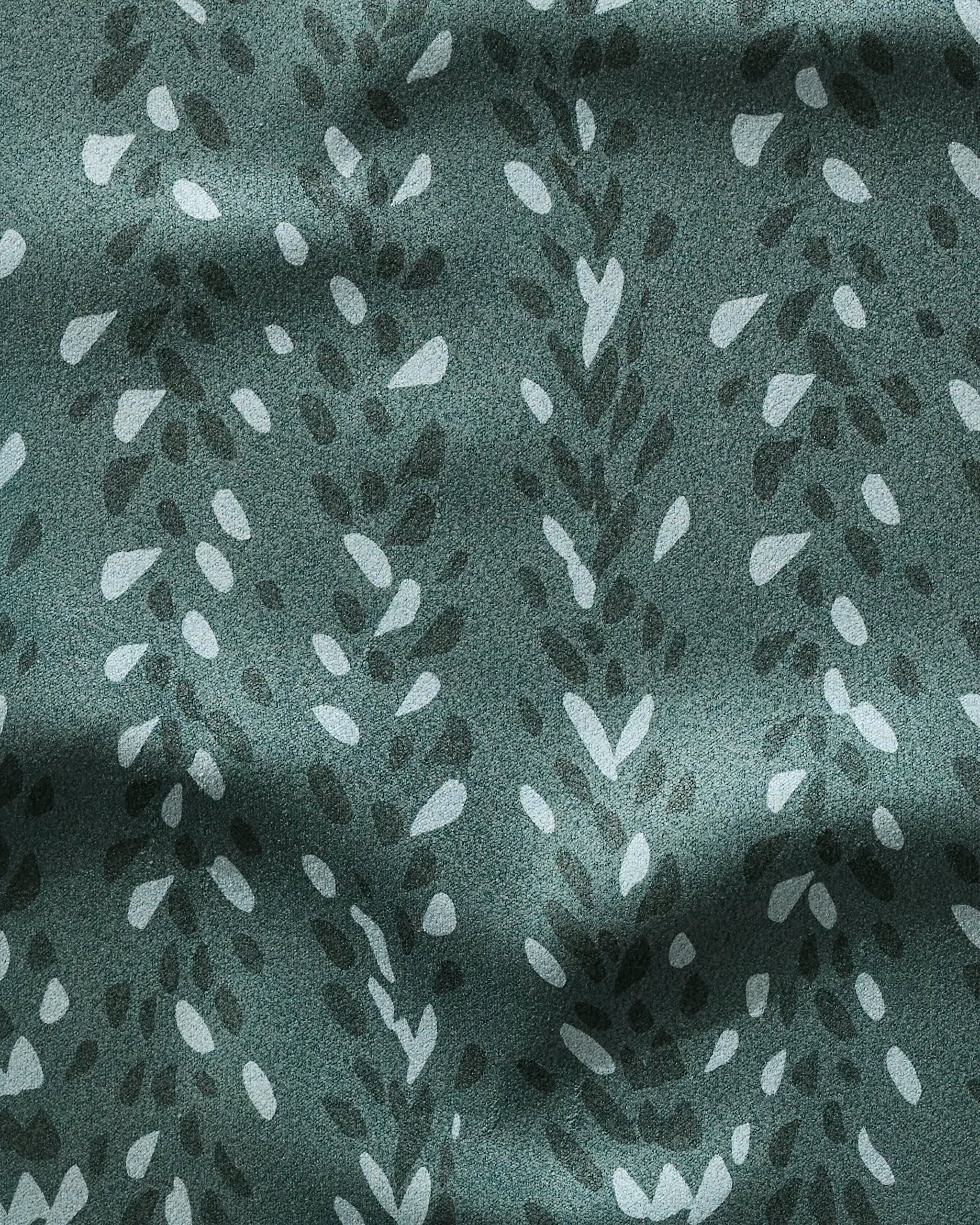 A close-up of Pose fabric by GEOMETRY shows a green, leafy botanical pattern in varied shades on soft, matte recycled material with slight wrinkles for a textured appearance.
