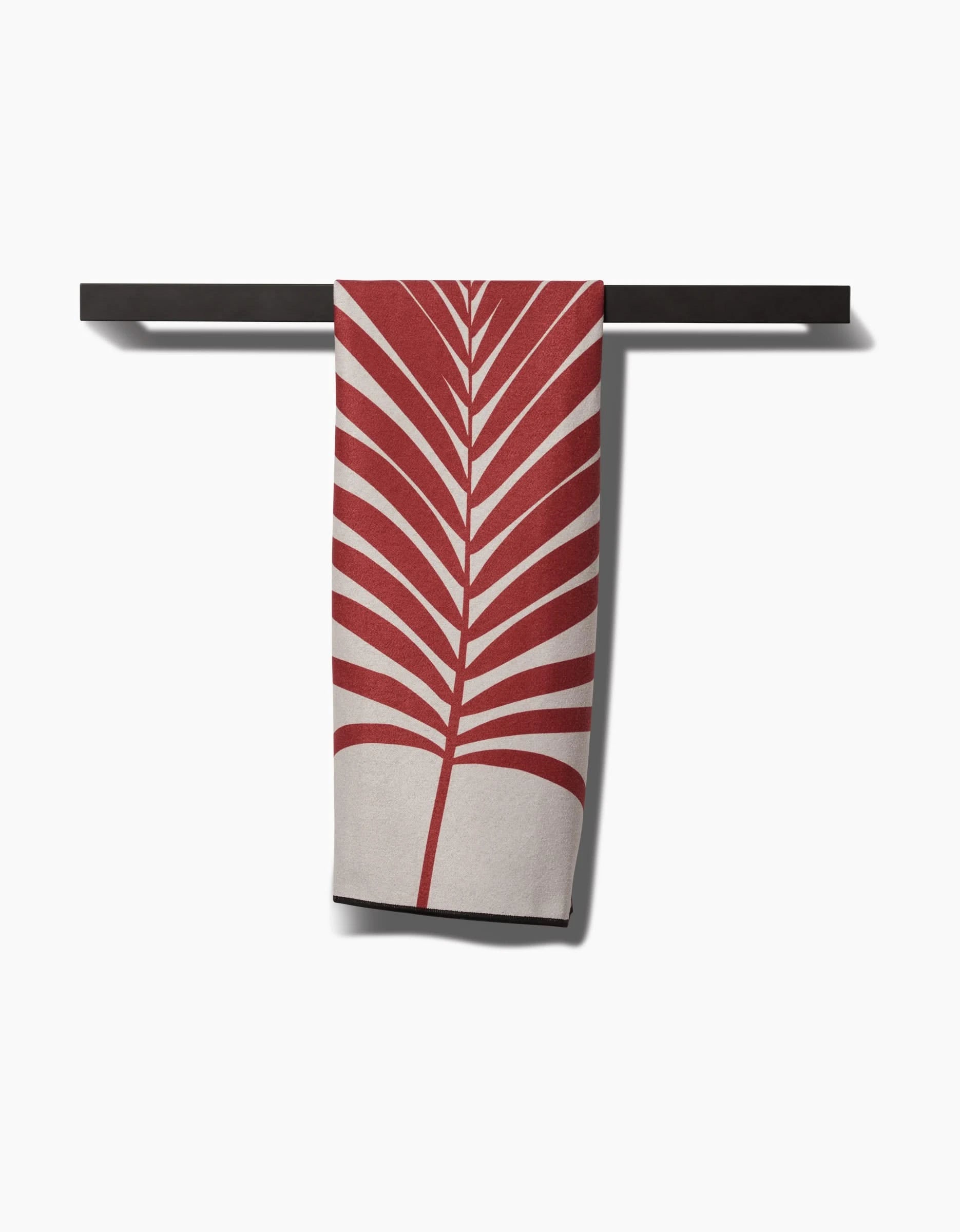 PrintedPlants Red Palm towel, made from recycled materials and featuring a bold red palm leaf on beige, hangs neatly over a black towel bar against a white background.