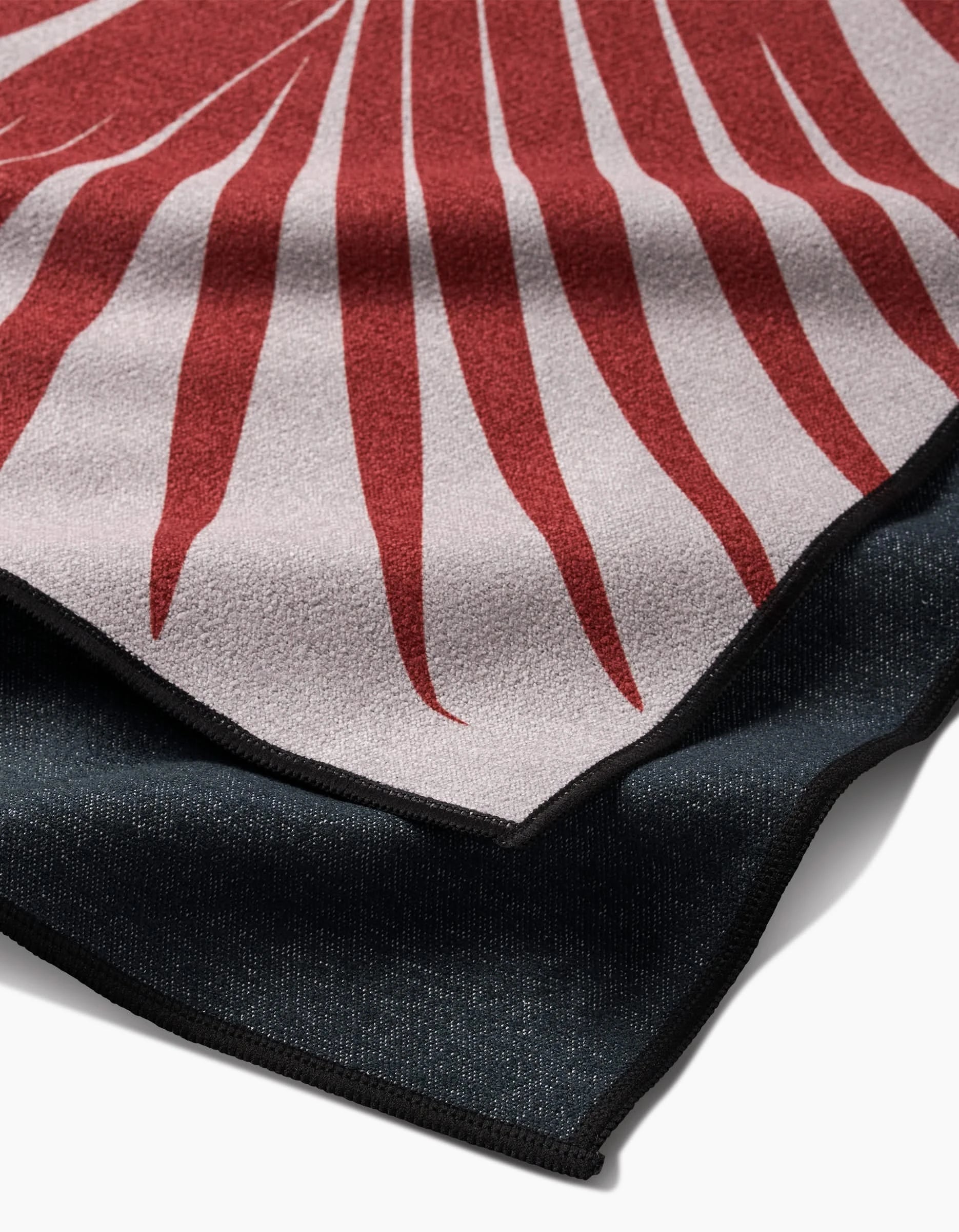 A close-up of two stacked PrintedPlant Red Palm fitness towels: the top features light gray with bold red, radiating lines; the bottom is solid black Geoweave Fabric. Both have sleek black edging.