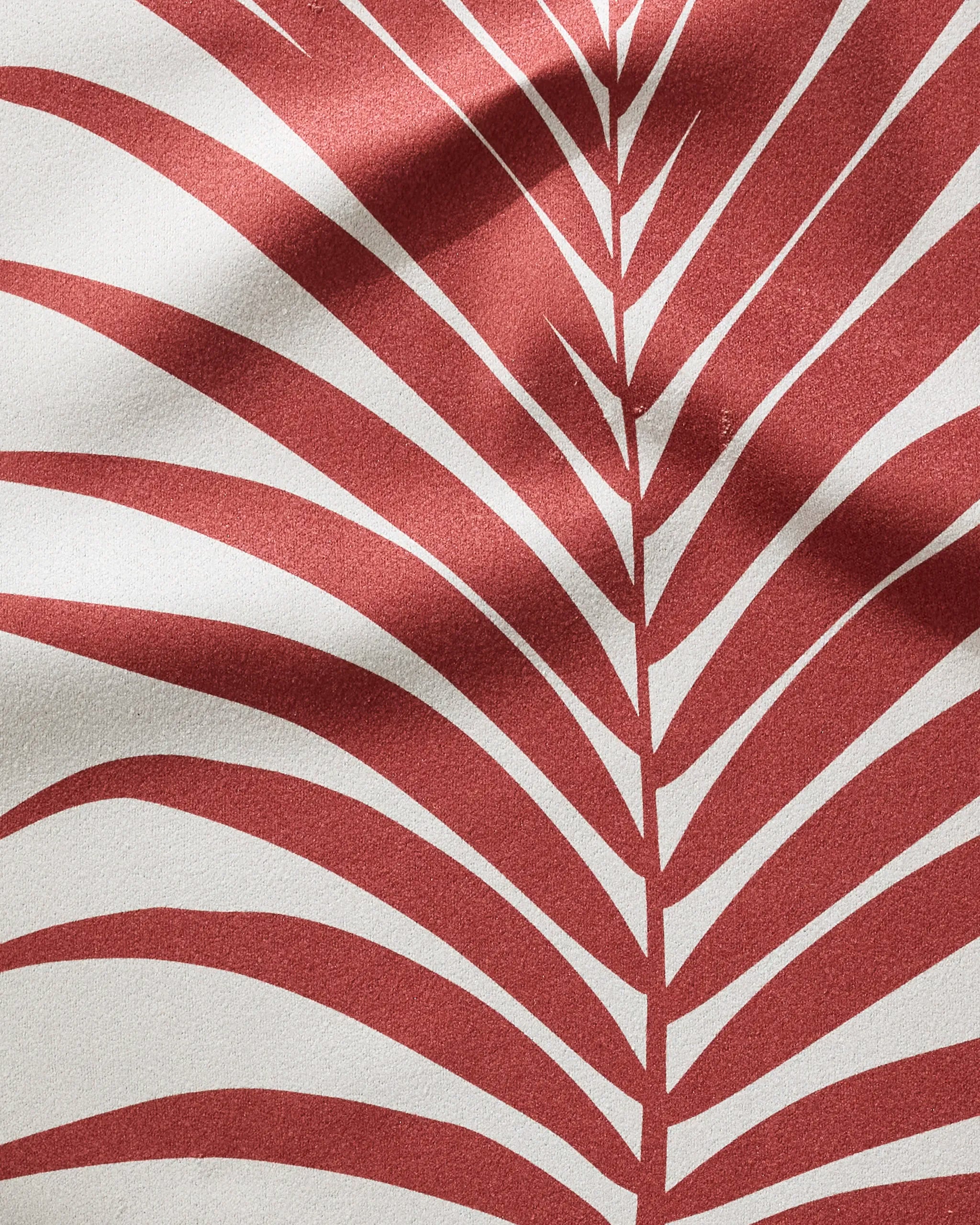 Close-up of PrintedPlant's Red Palm: a red palm leaf pattern on textured white, crafted from ultra-absorbent recycled materials. Light and shadow create soft curves across the eco-friendly design.