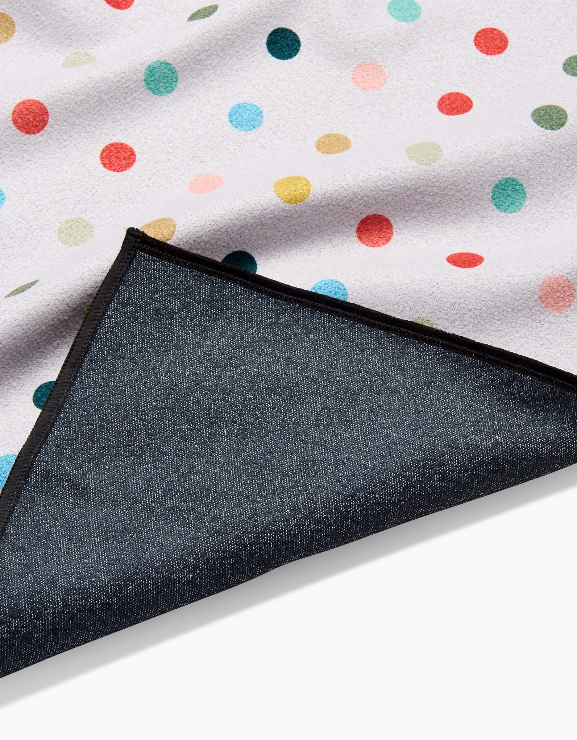 A close-up of the Elizabeth Edwards Retro Dot Fitness Towel in white with colorful red, yellow, blue, and green polka dots. One corner is folded to show its ultra-absorbent dark underside and black edging.