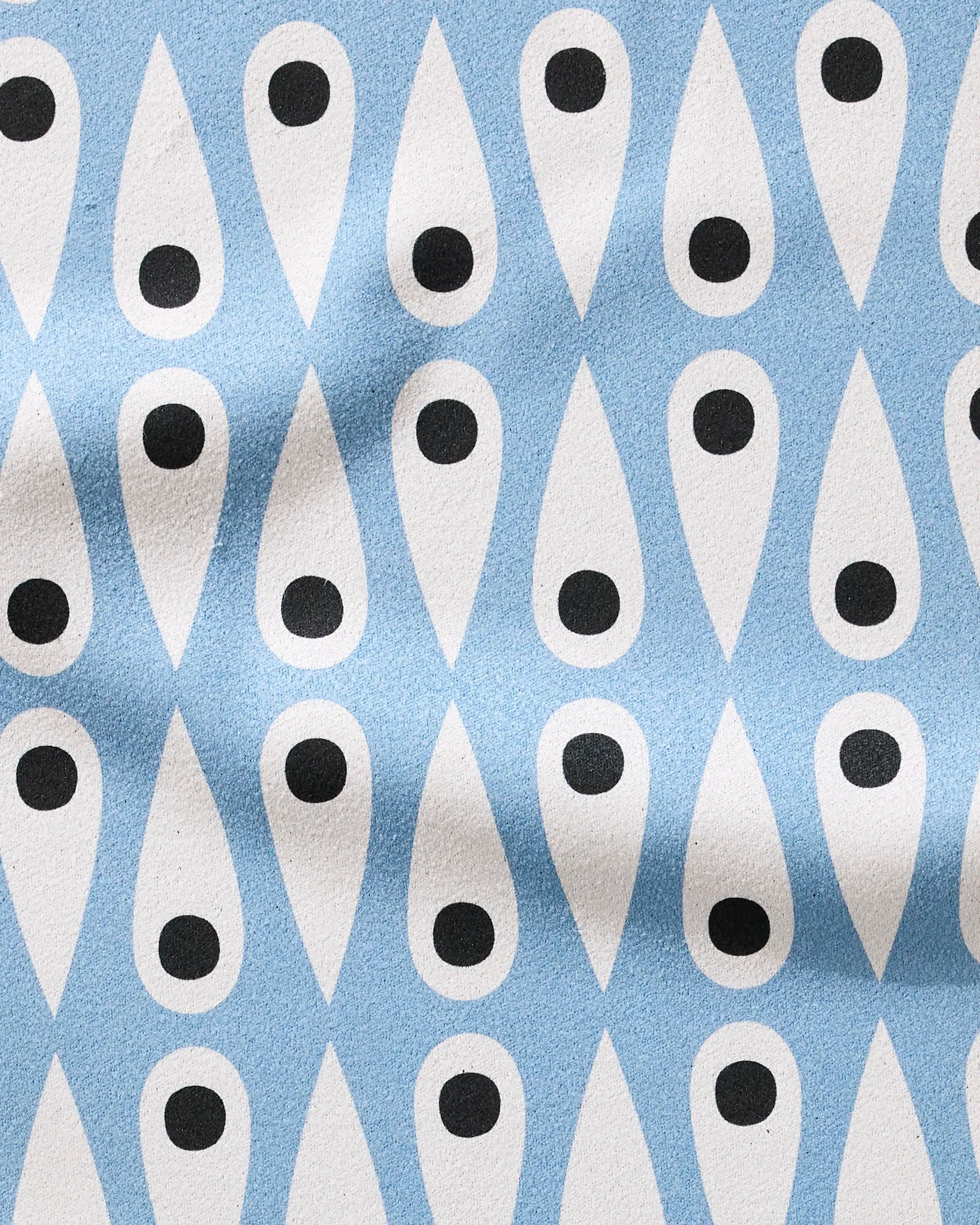 Retro Rain by Anette Heiberg is a recycled fabric featuring white teardrop shapes with black dots, arranged in rows on a light blue background with soft, natural folds.