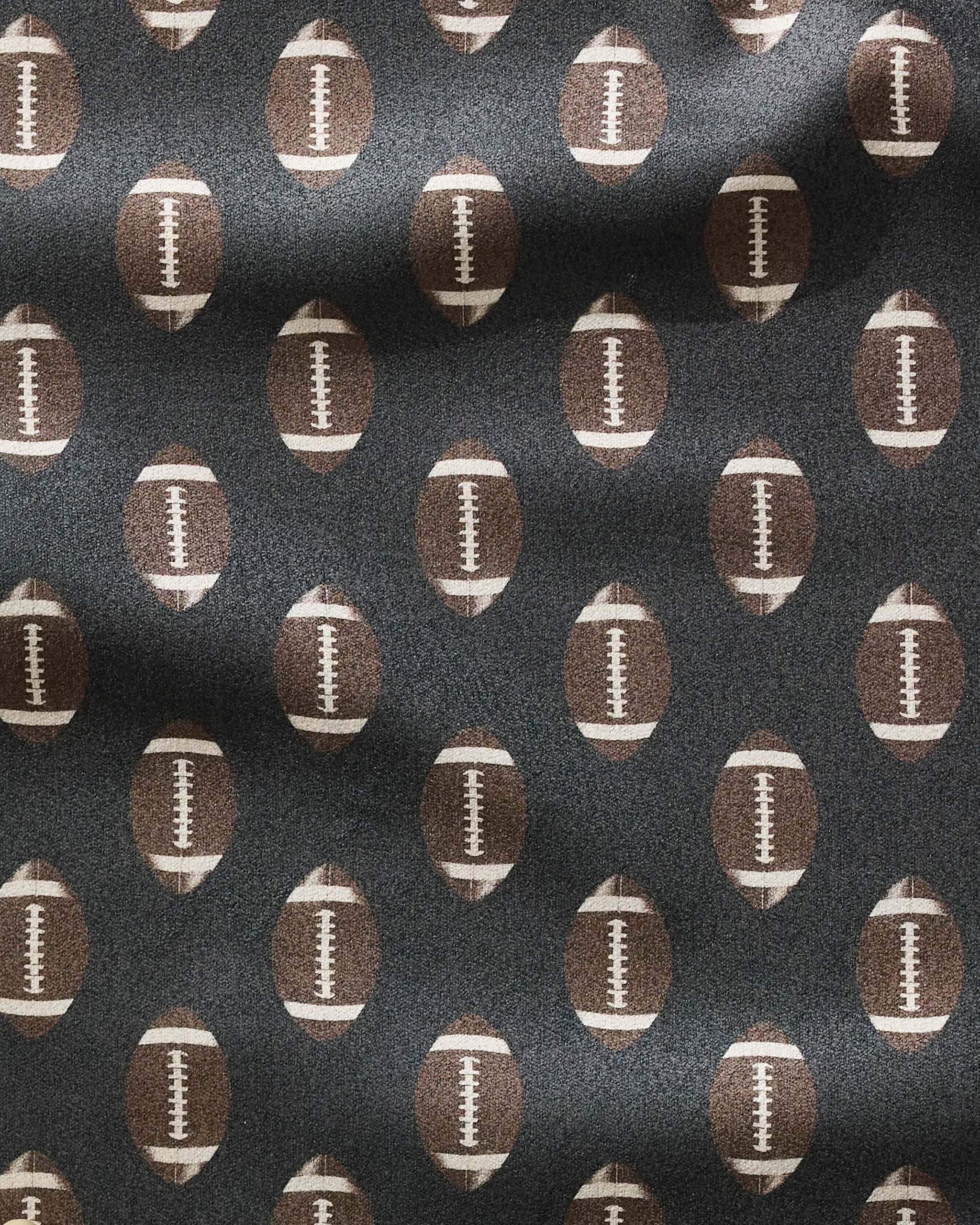 A close-up of the Geometry Rush fitness towel, featuring a pattern of evenly spaced brown and white American footballs on a dark background, with gentle folds and shadows highlighting its ultra-absorbent design.