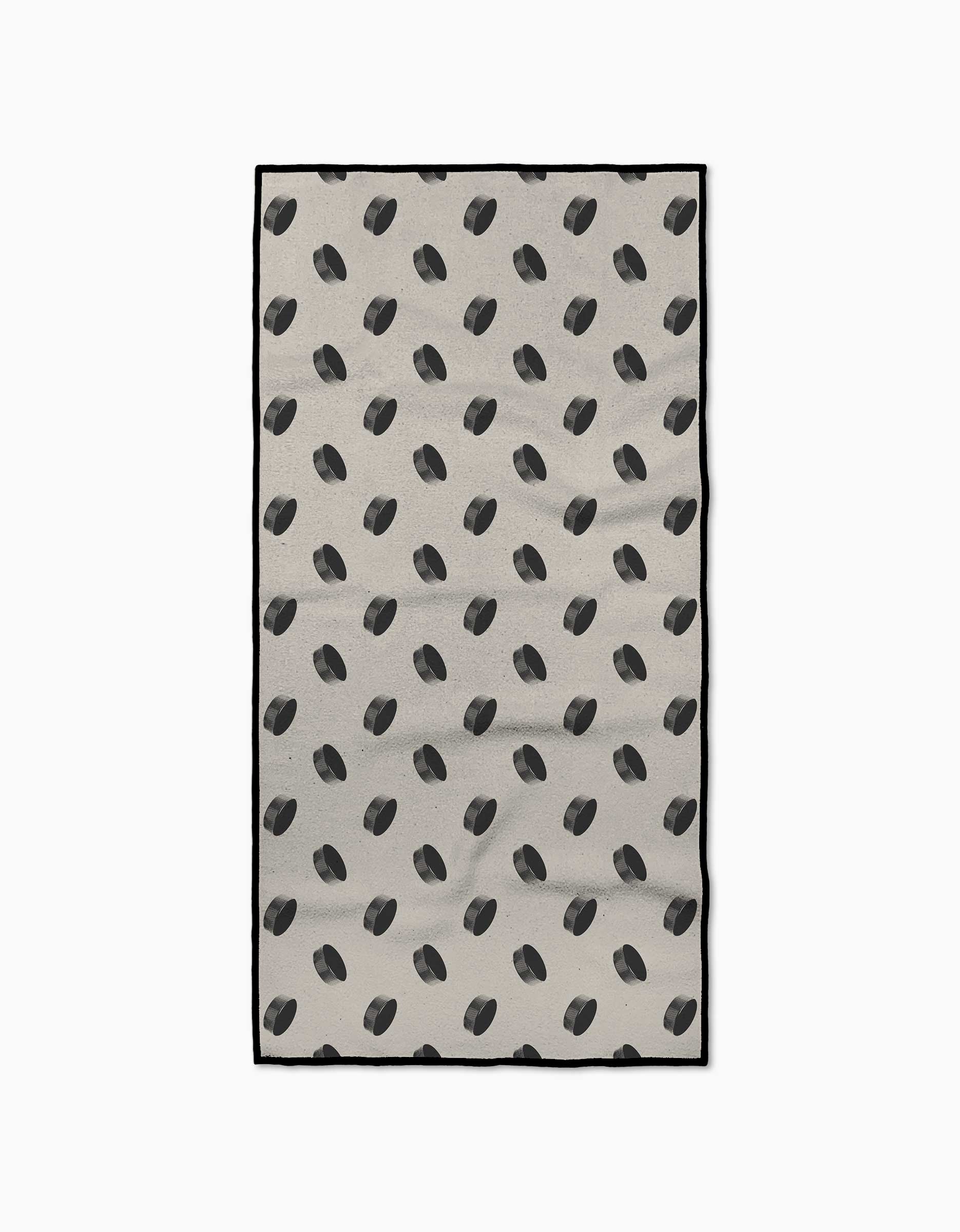 The Geometry Slapshot rectangular beige rug is made from recycled materials and features a repeating pattern of scattered black hockey pucks as seen from above.